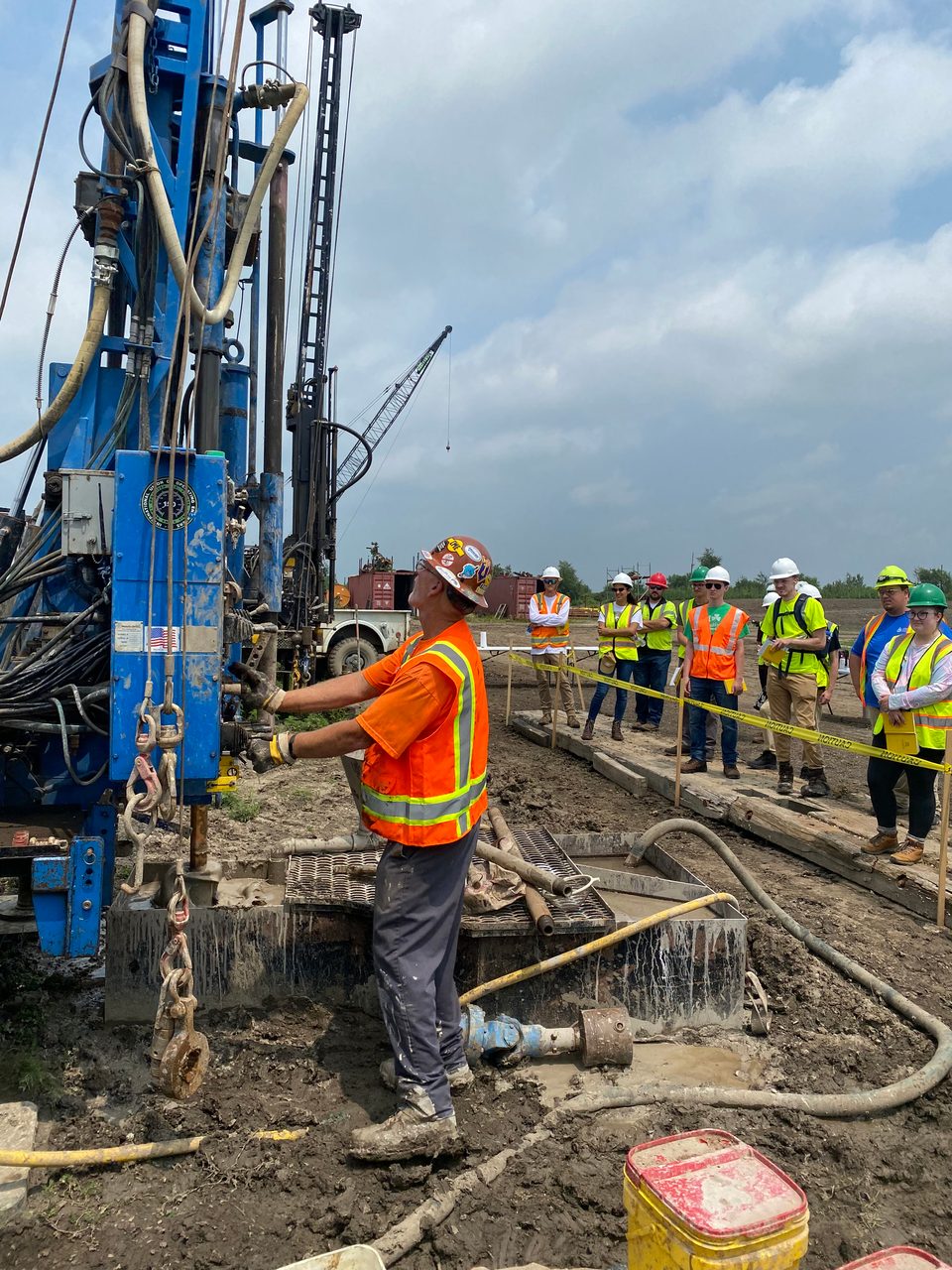 High-visibility clothing, Hard hat, Road surface, Sky, Workwear, Cloud, Asphalt, Yellow, Tree