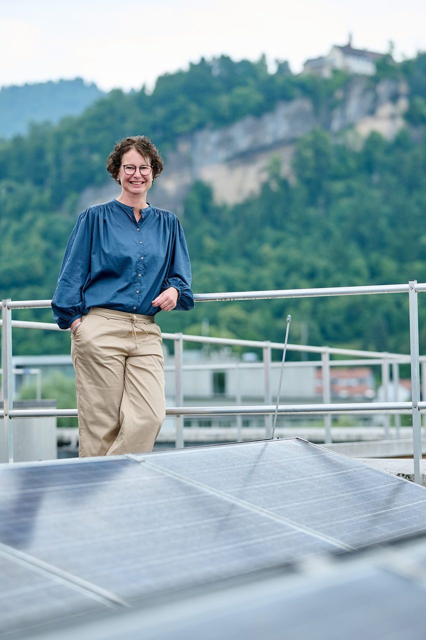 Smiling woman in glasses on a rooftop, with solar panels and distant mountains.