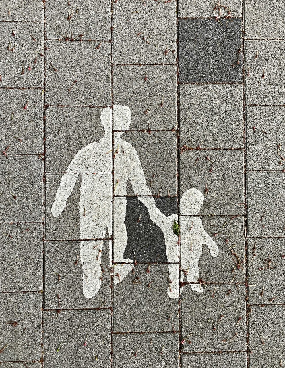 A white stencil of an adult and child holding hands on grey paving stones.