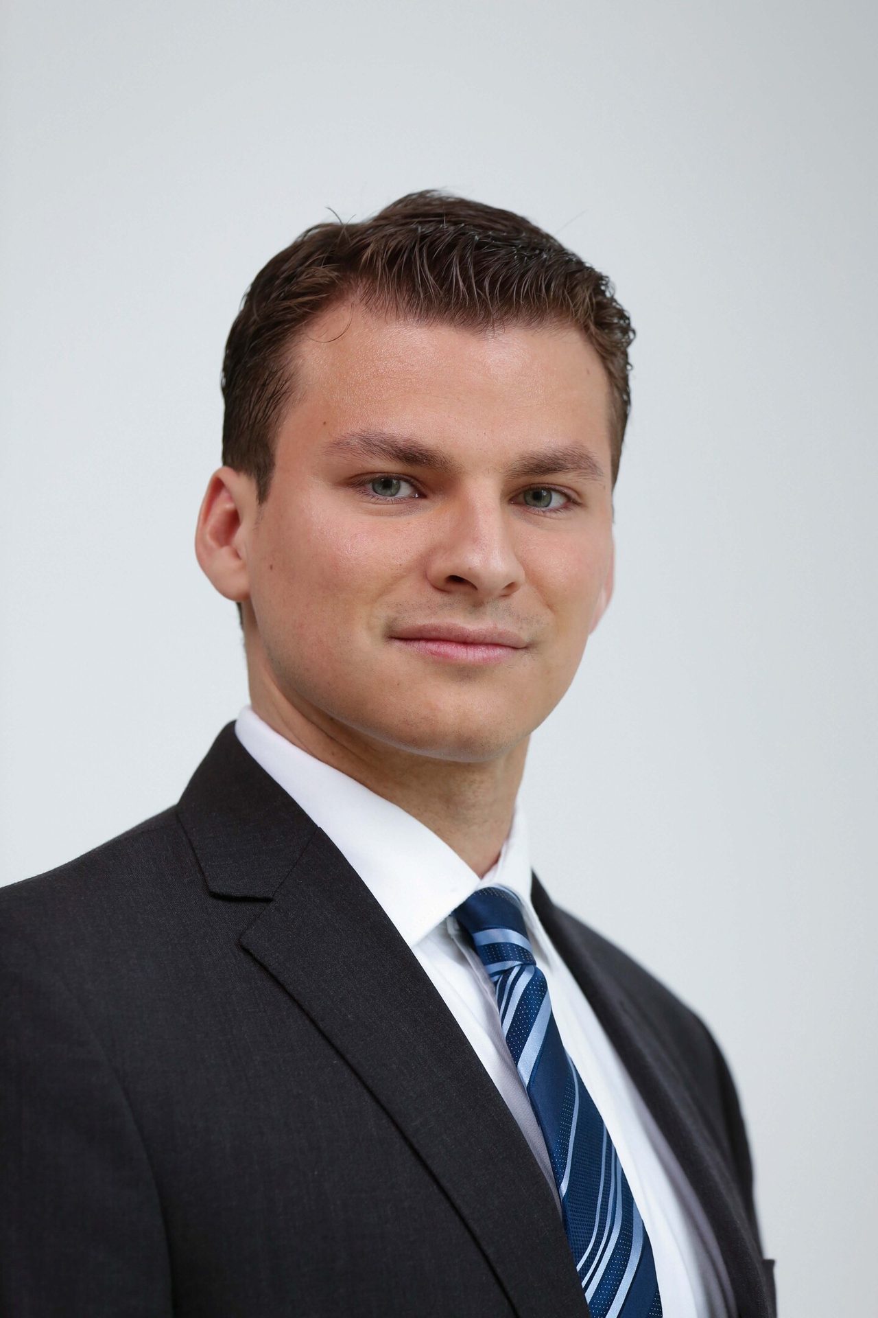 Professional headshot of a smiling man in a dark suit and blue tie.