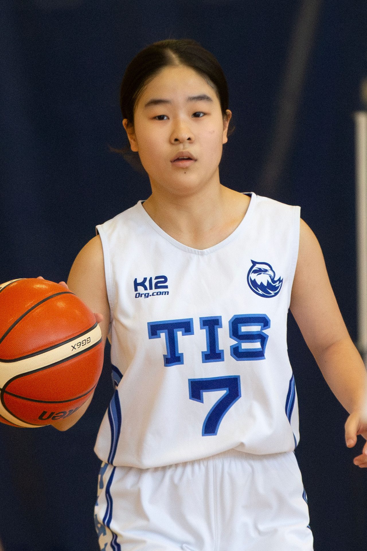 A young Asian female basketball player in uniform, holding a basketball.