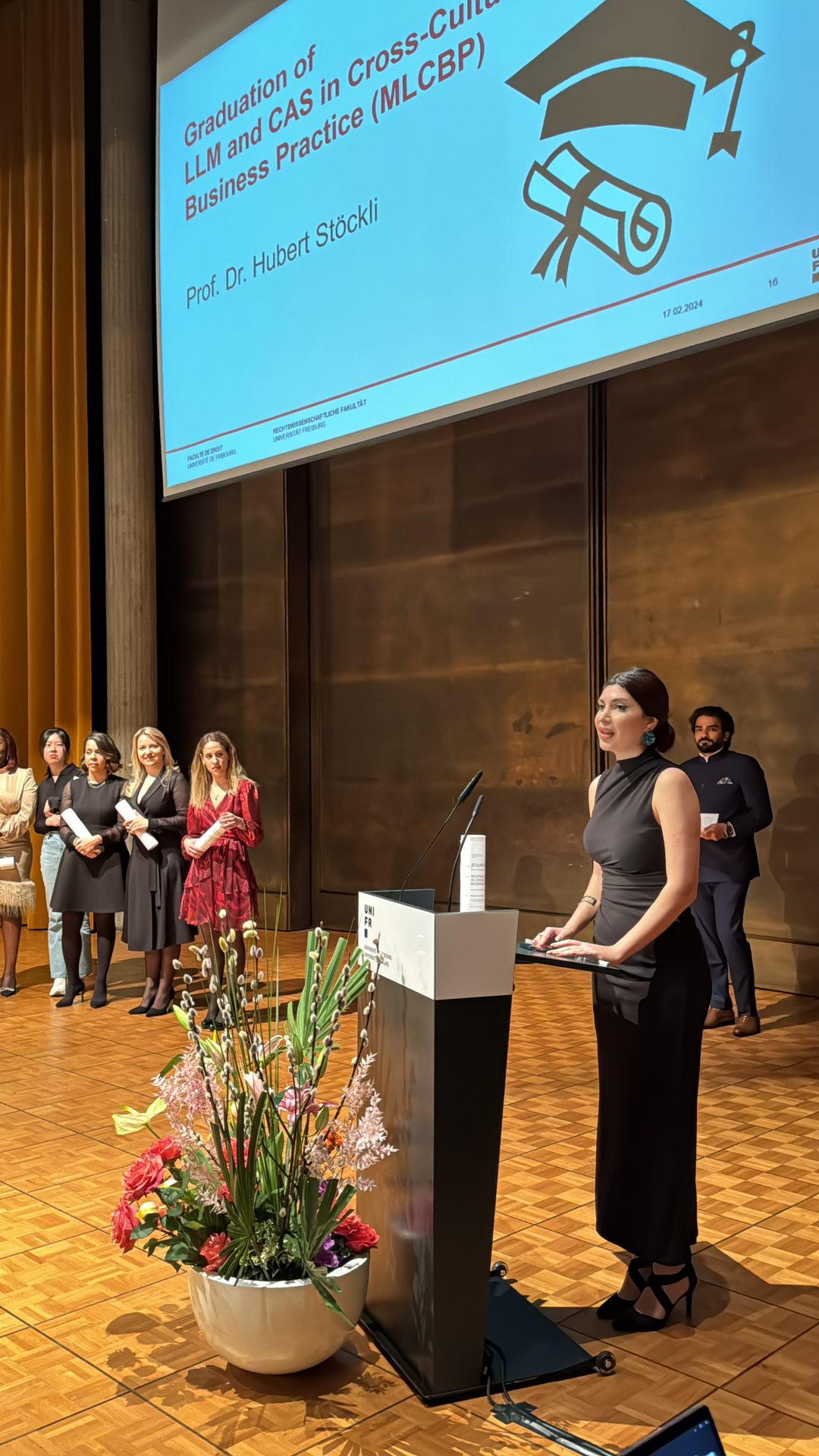 Graduation for LLM and CAS program, speaker at podium, graduates in background.