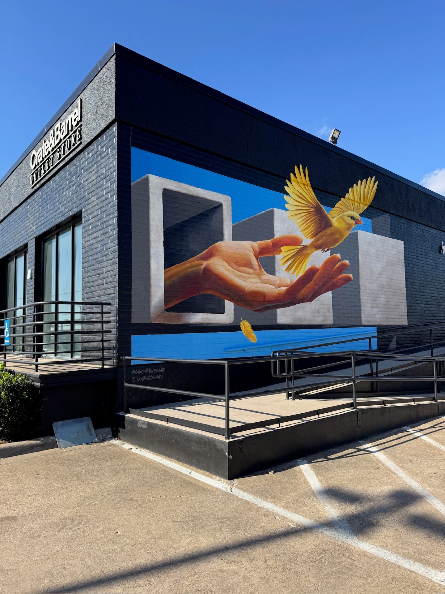 Mural on Crate & Barrel store: hand releasing a yellow bird from abstract shapes.