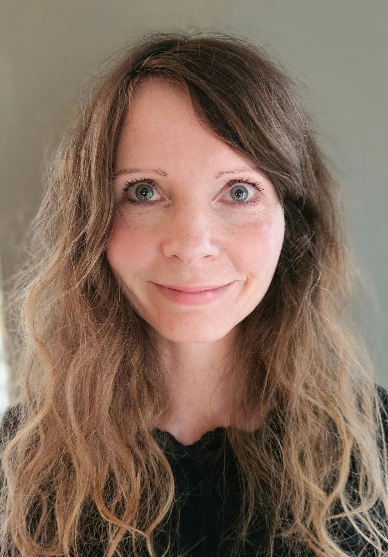 Close-up of a smiling woman with long wavy hair and light eyes.