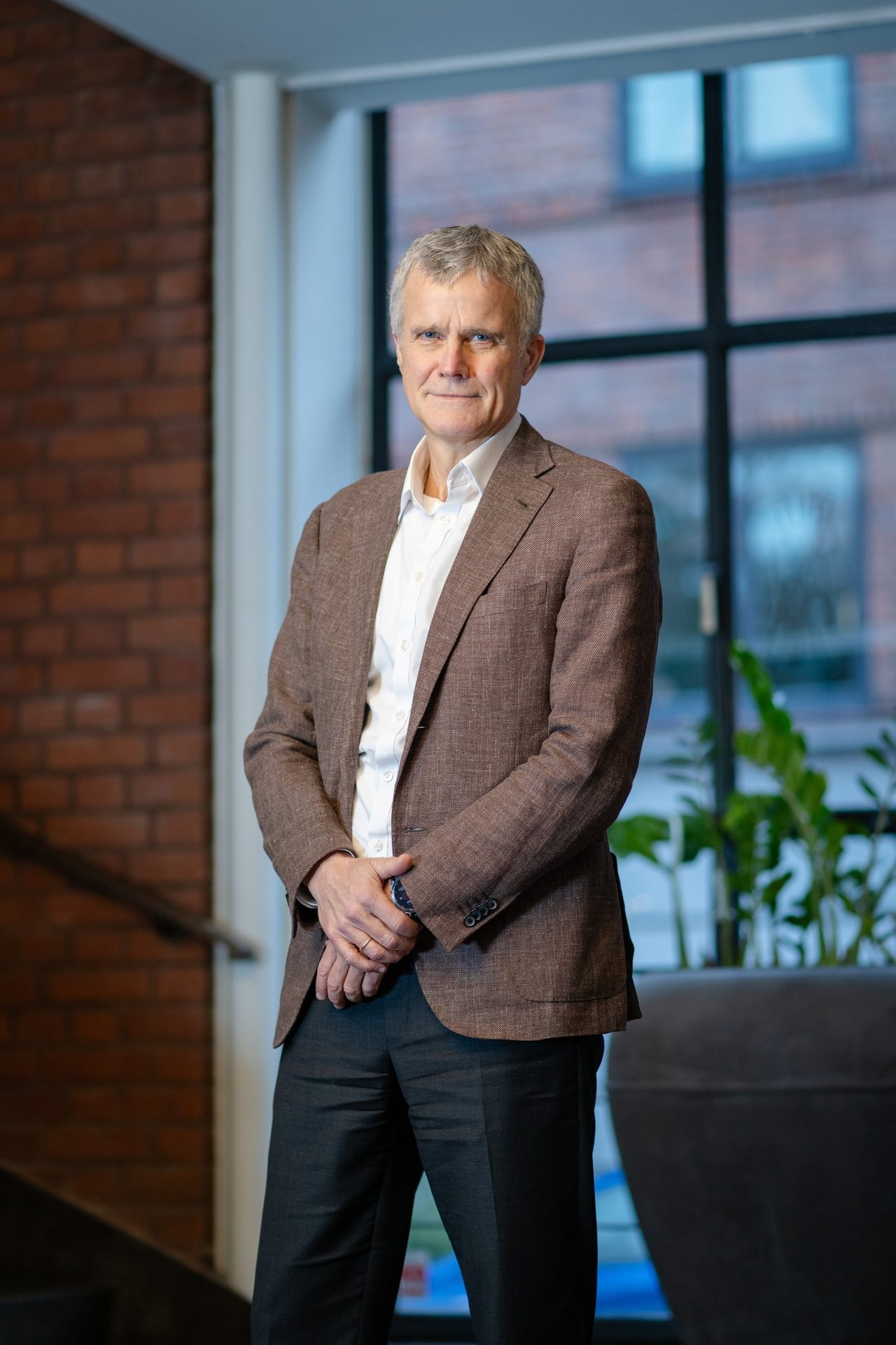 Portrait of a smiling man with gray hair, wearing a brown blazer and white shirt.