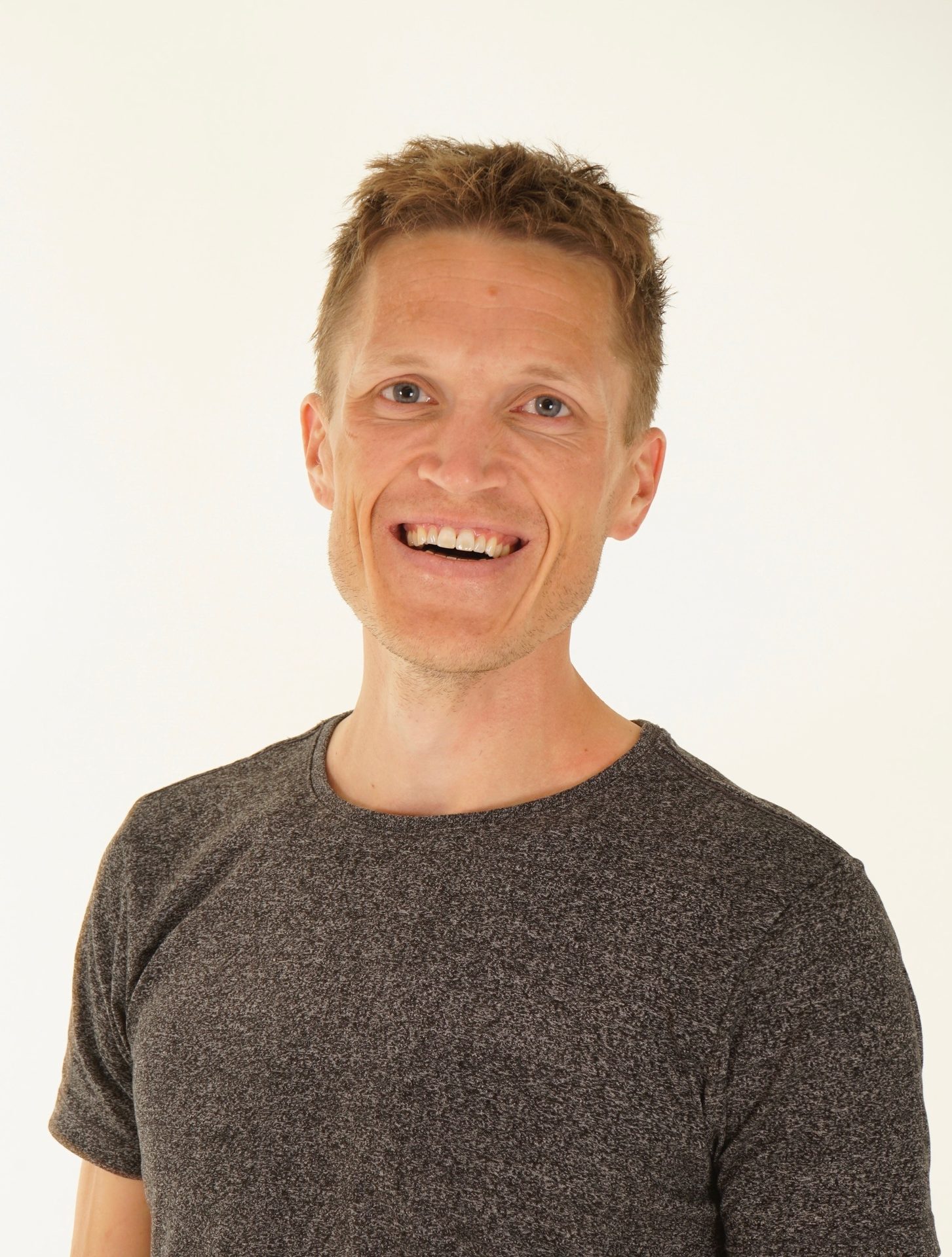 Smiling man in a grey t-shirt on a white background.