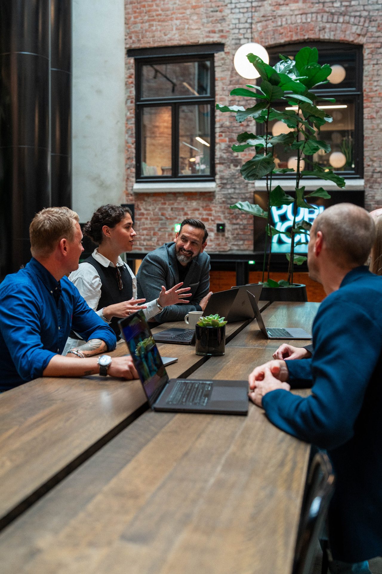 Four people are discussing around a table with laptops in a modern office.