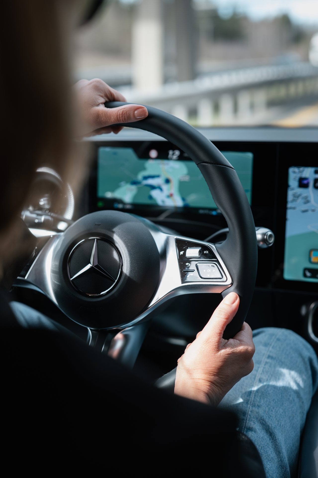A person's hands on a Mercedes-Benz steering wheel, with navigation displayed on the dashboard.