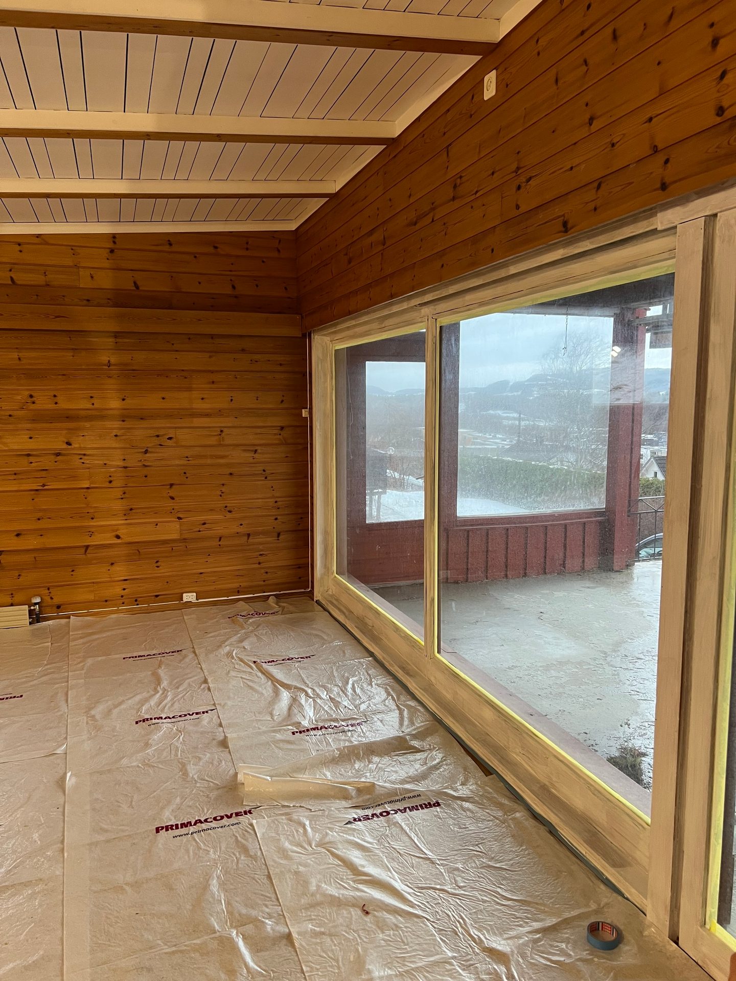 Warm wood paneled room interior with white ceiling, large sliding glass door, and protected floor.