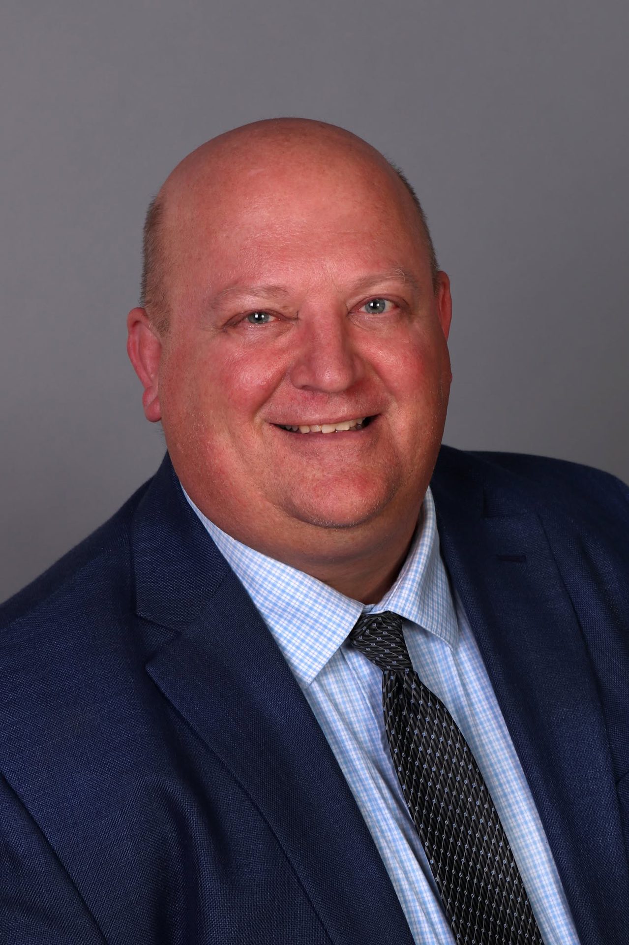 Smiling bald man in a blue suit, plaid shirt, and tie.