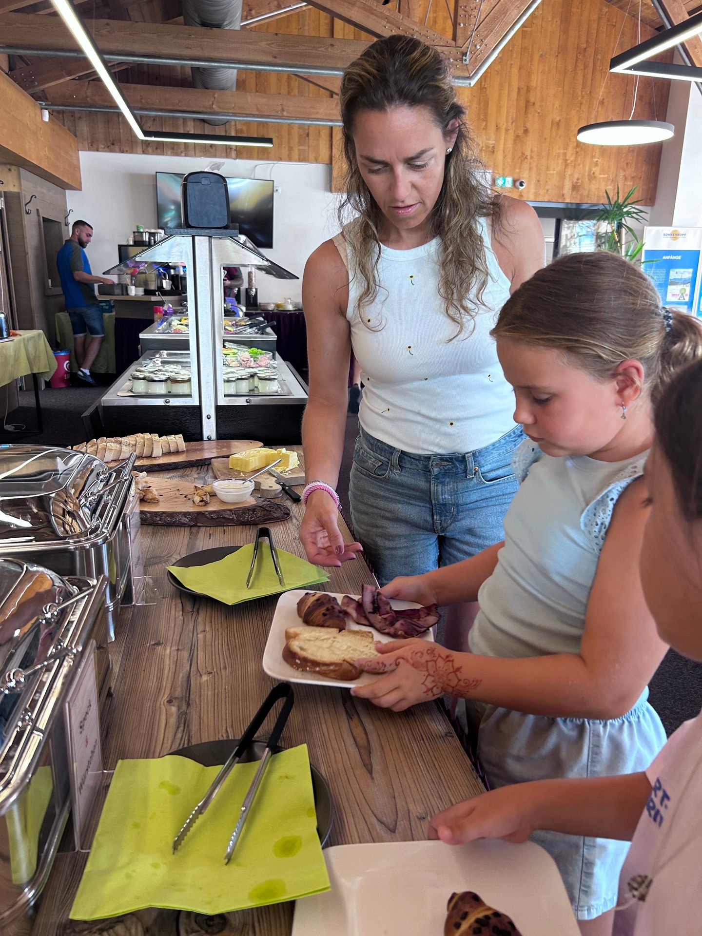 A woman and a girl are selecting food from a buffet table, with the girl holding a plate.