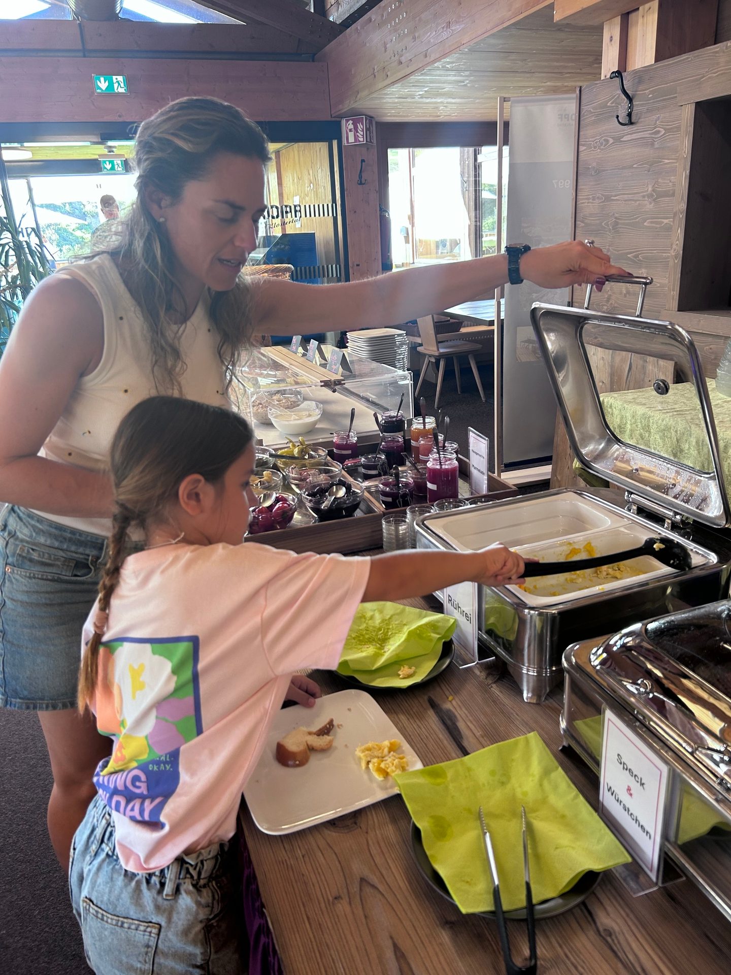 A woman and a child are serving themselves food from a breakfast buffet.