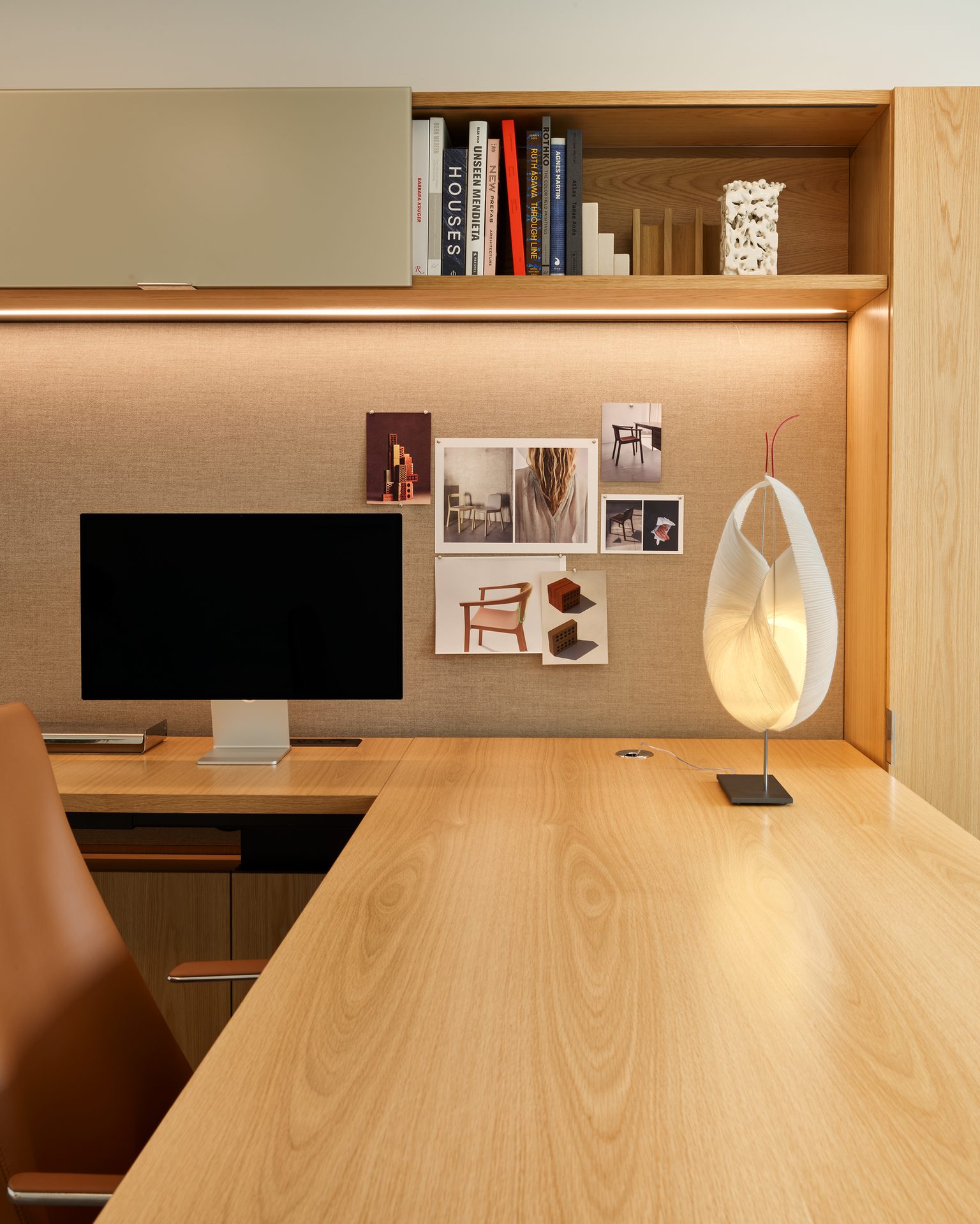 A modern, organized wooden home office corner with a desk, computer, books, and a sculptural lamp.