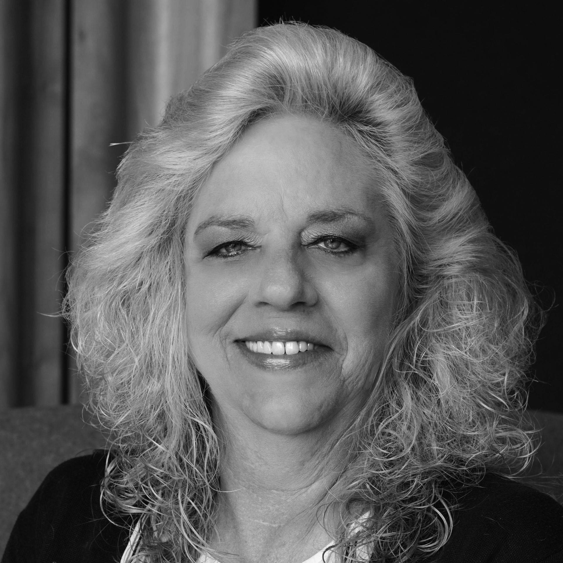 B&W headshot of a smiling older woman with long, curly grey hair.