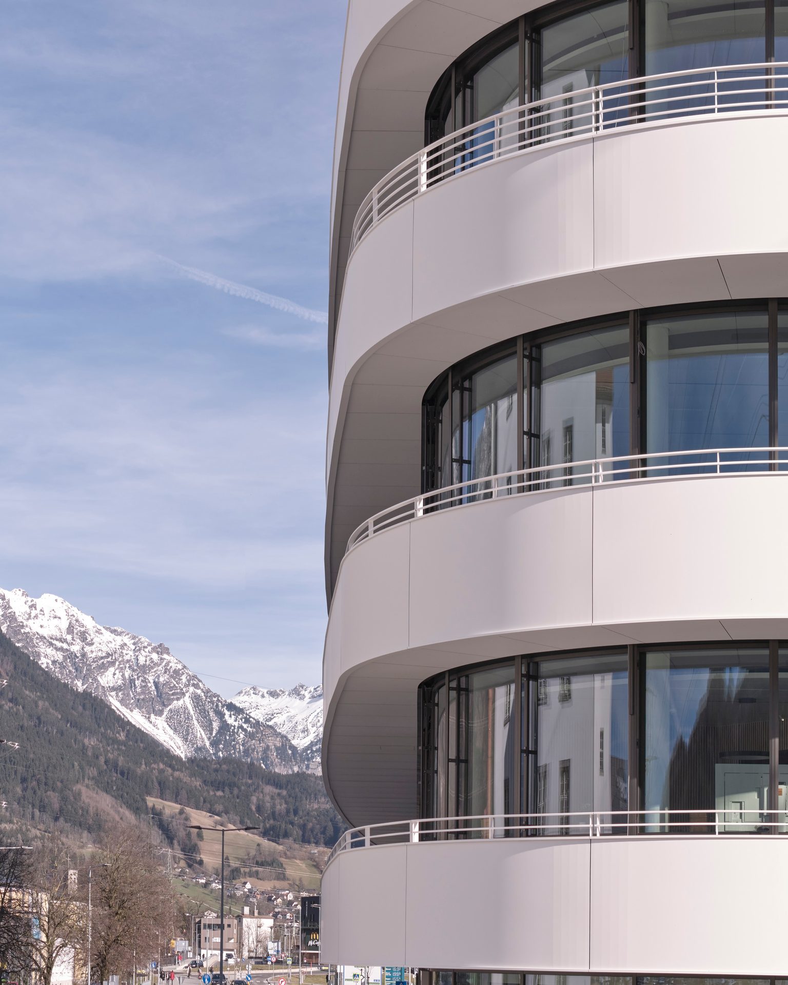 Modern building with curved balconies and reflective windows, set against a backdrop of snowy mountains.