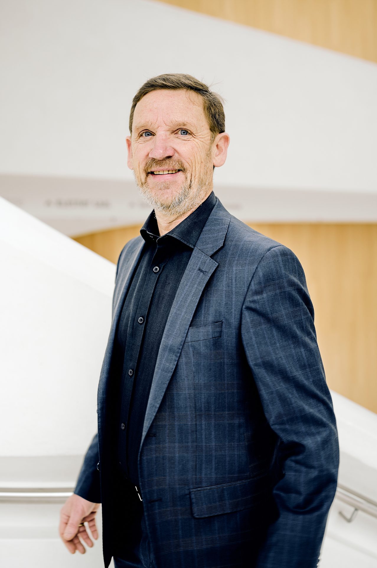 Smiling man with blue eyes and beard in a blue plaid suit jacket.