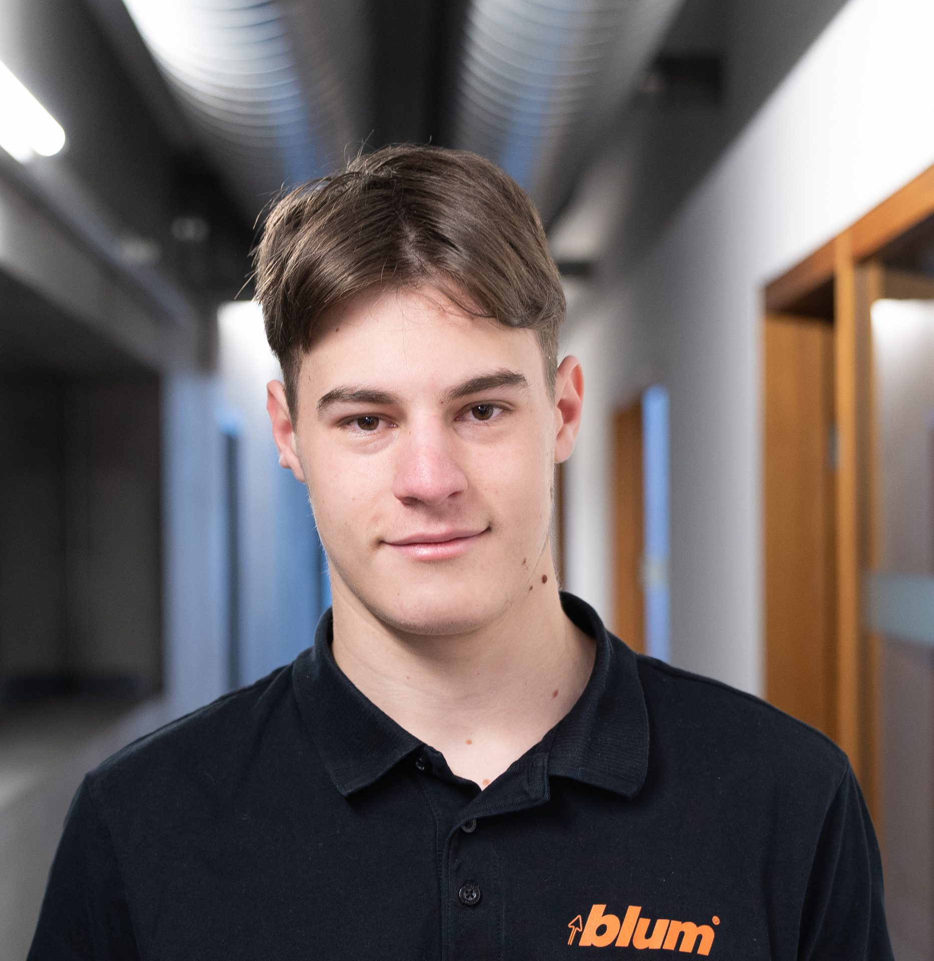 Young man smiling, wearing a black Blum polo shirt.