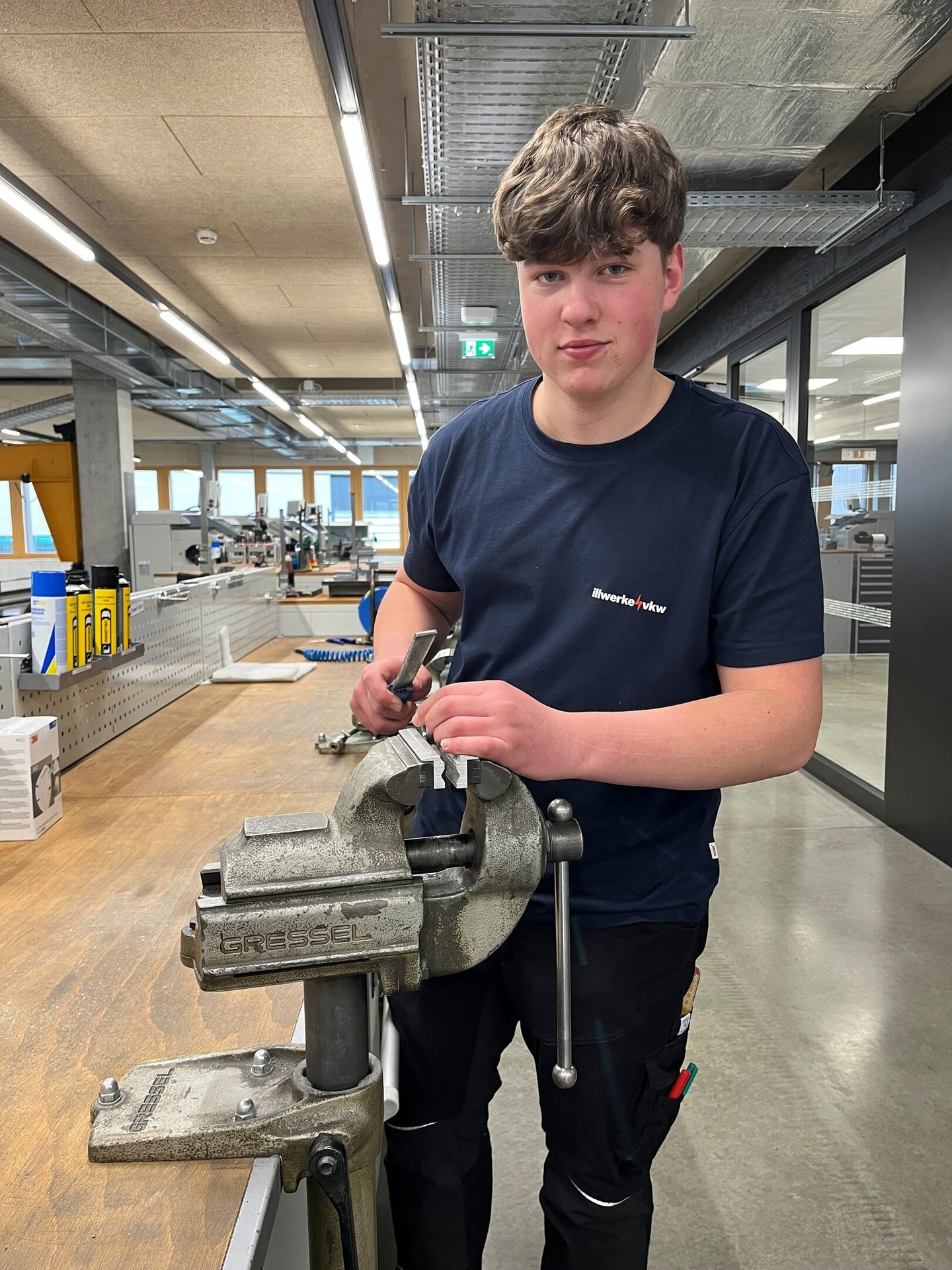 Young man shaping metal with a tool at a workshop vise.