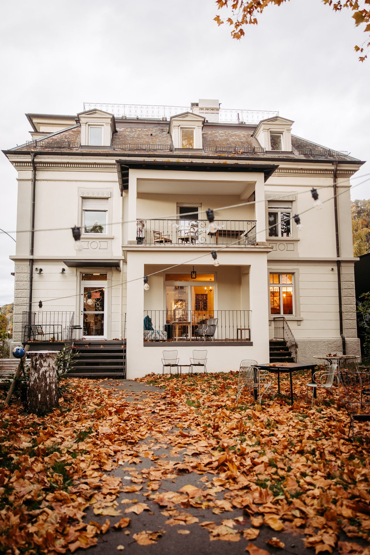 Elegant building with balconies and dormers, autumn leaves on the ground.