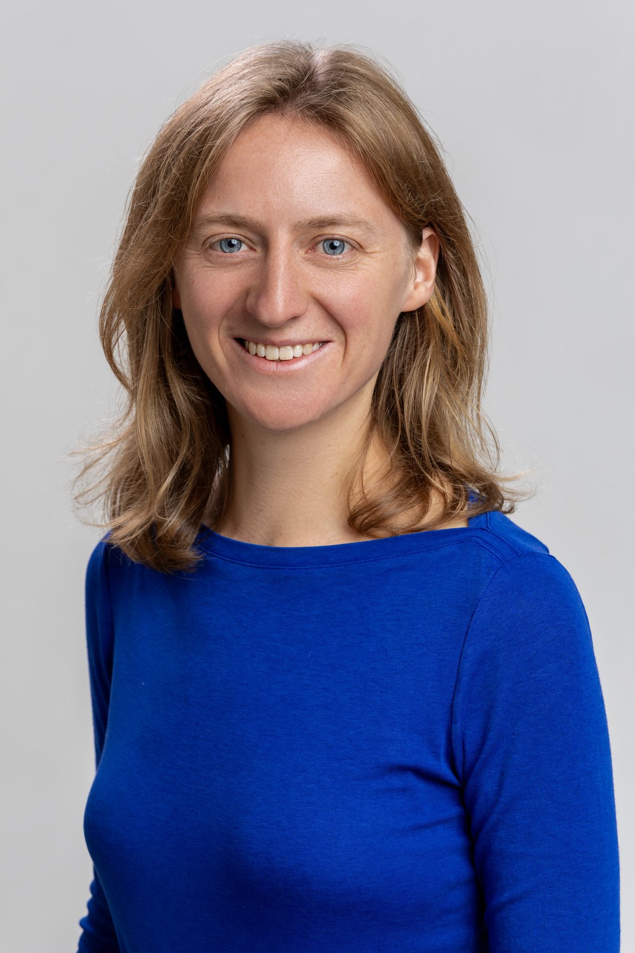 Smiling woman with blond hair and blue eyes wearing a blue long-sleeved shirt.