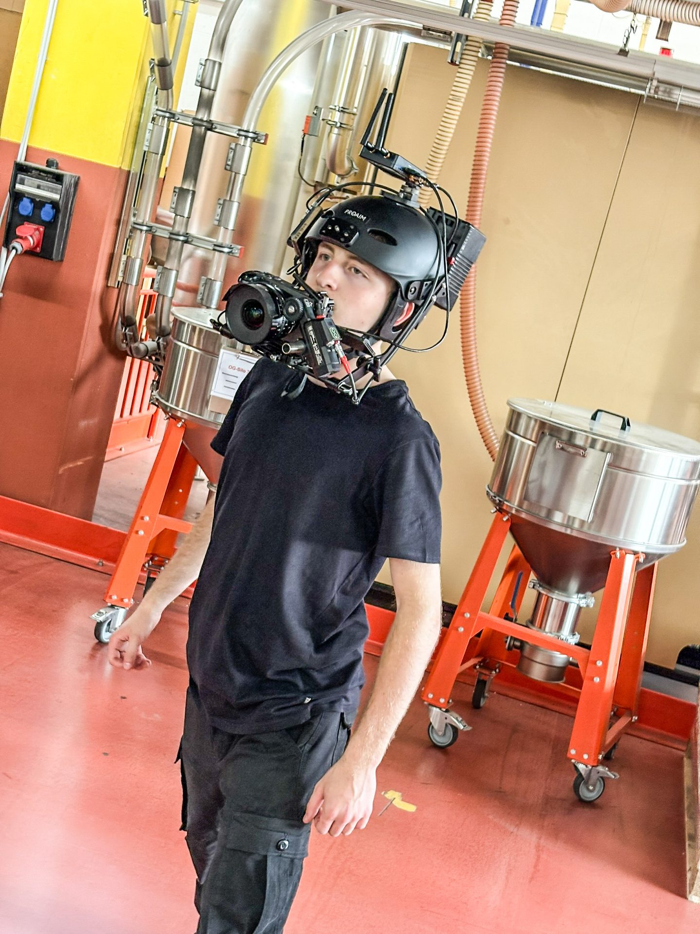 Person wearing a camera-mounted helmet in an industrial facility with metal machinery.