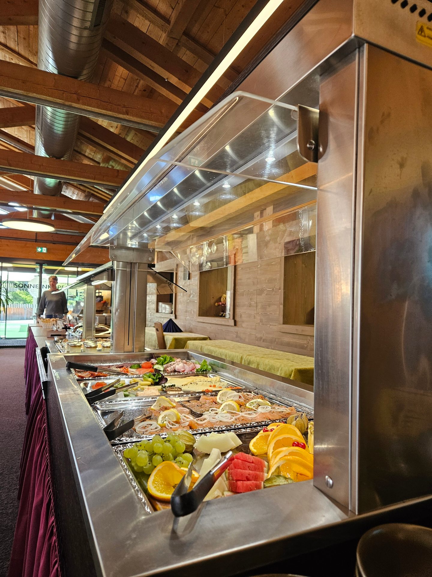 A long buffet line with fresh fruit, sliced salmon, cold cuts, and salads.