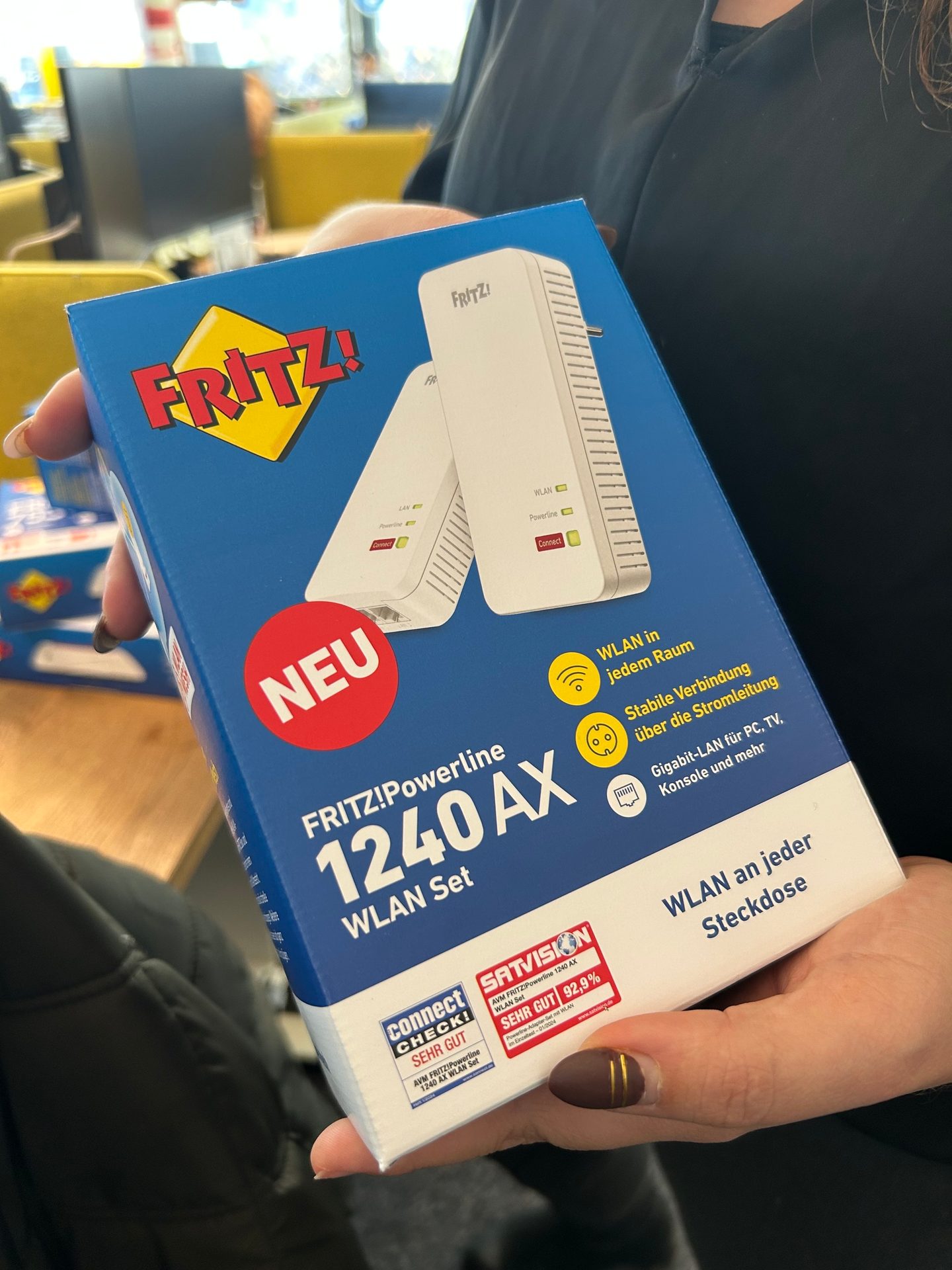 Hands holding a FRITZ!Powerline 1240 AX WLAN Set box, featuring "NEW" and product details.