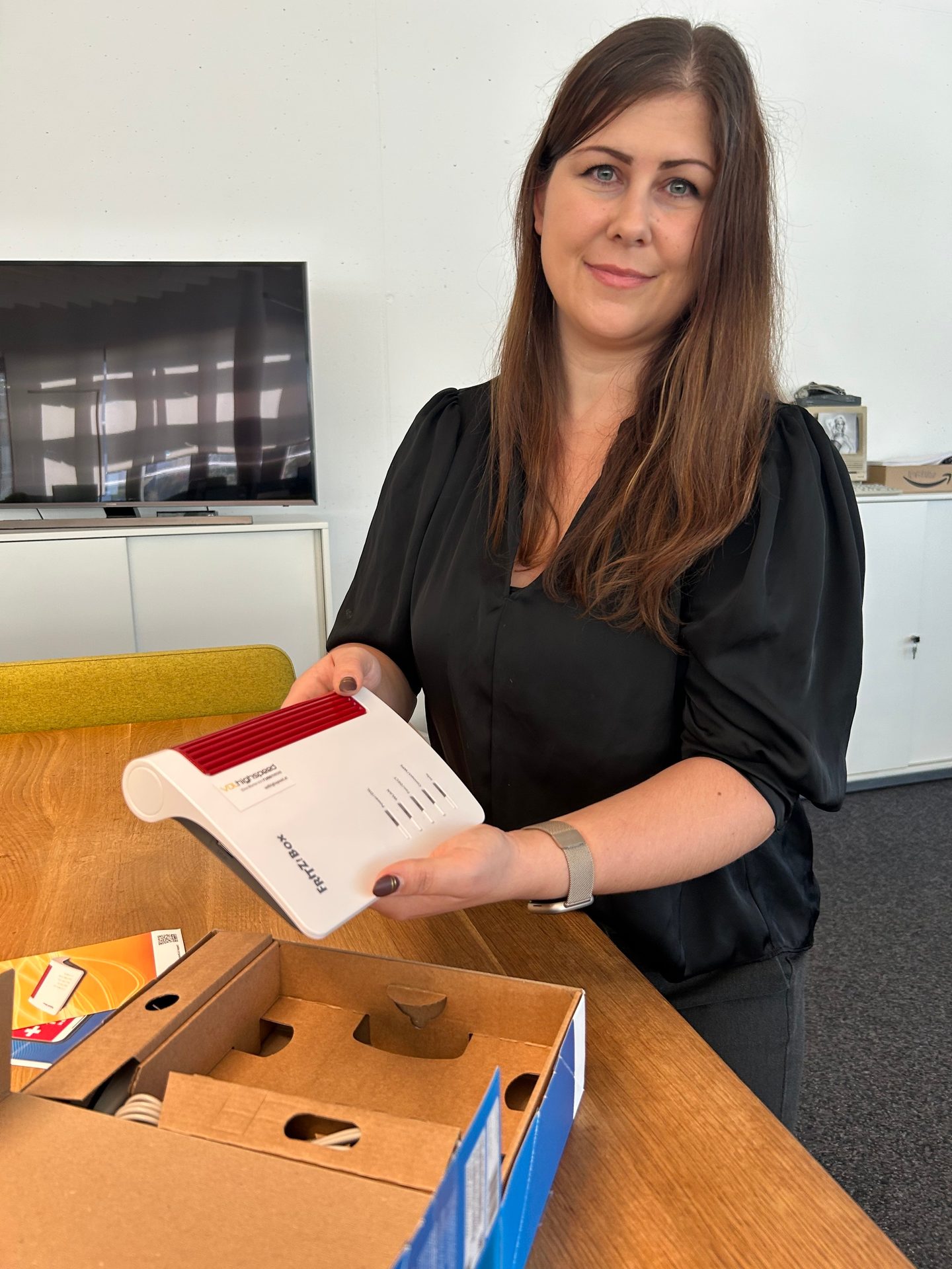 A woman holds a white FRITZ!Box router over an open box on a wooden table.