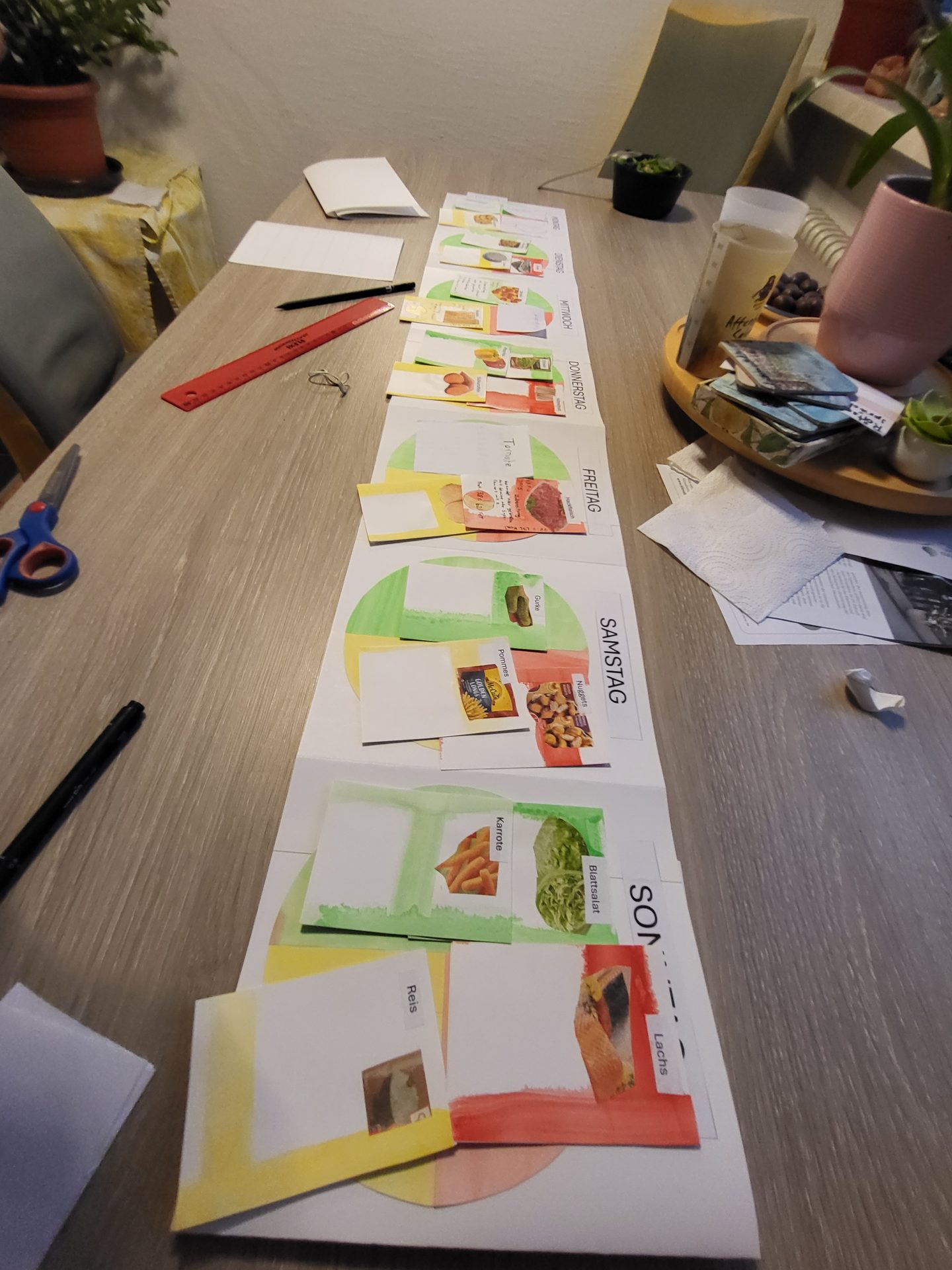 Handcrafted paper weekly meal planner with food cards and crafting tools on a wooden table.