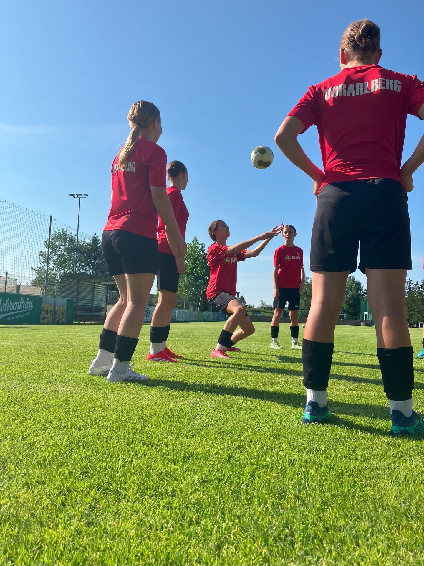 Girls in red shirts playing volleyball outdoors on a sunny day.