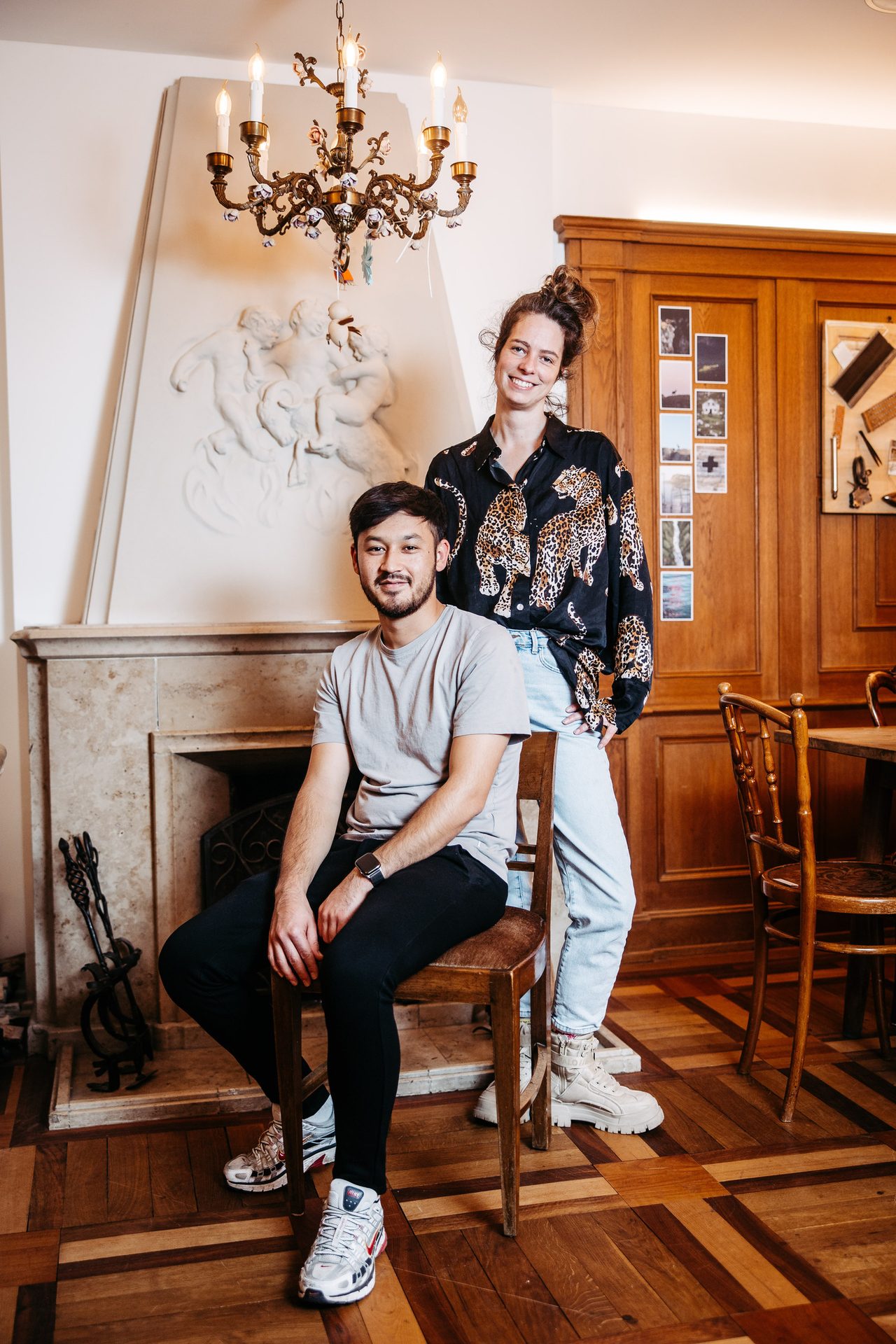 Man seated and woman standing, smiling in a room with a fireplace.