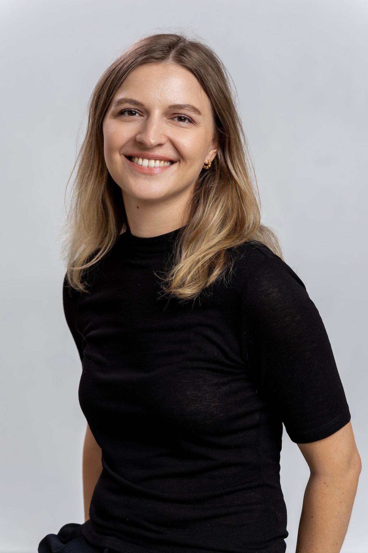 A smiling woman with blonde hair, wearing a black top, looking slightly to the right.