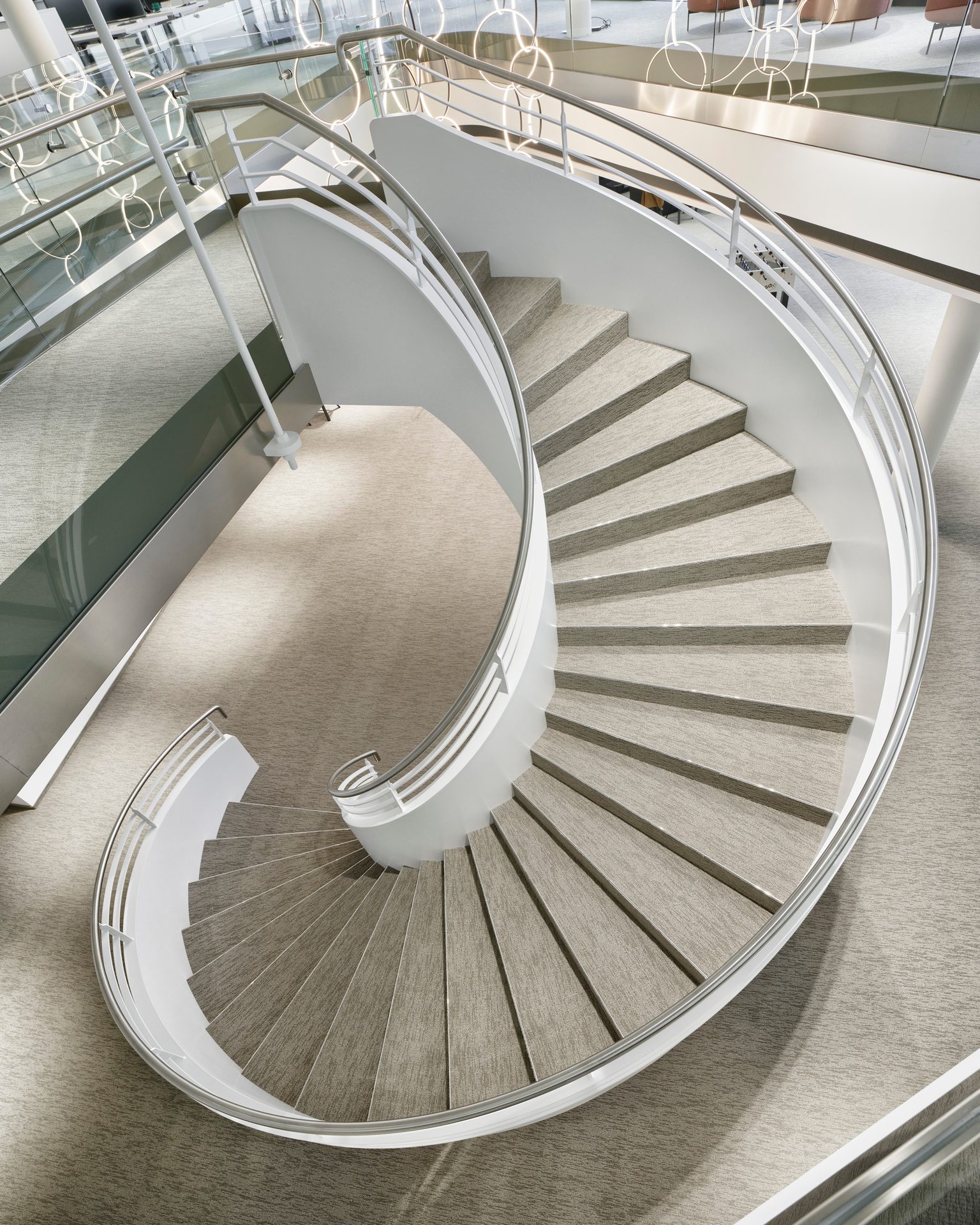 Modern, elegant spiral staircase with light carpeted steps and sleek white railings.