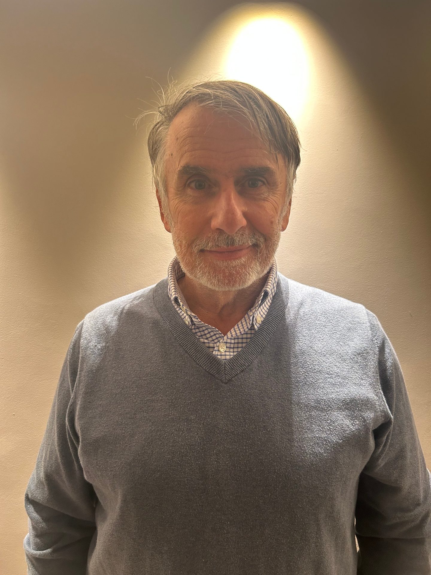 Smiling older man with beard and grey hair in a blue sweater and checkered shirt.
