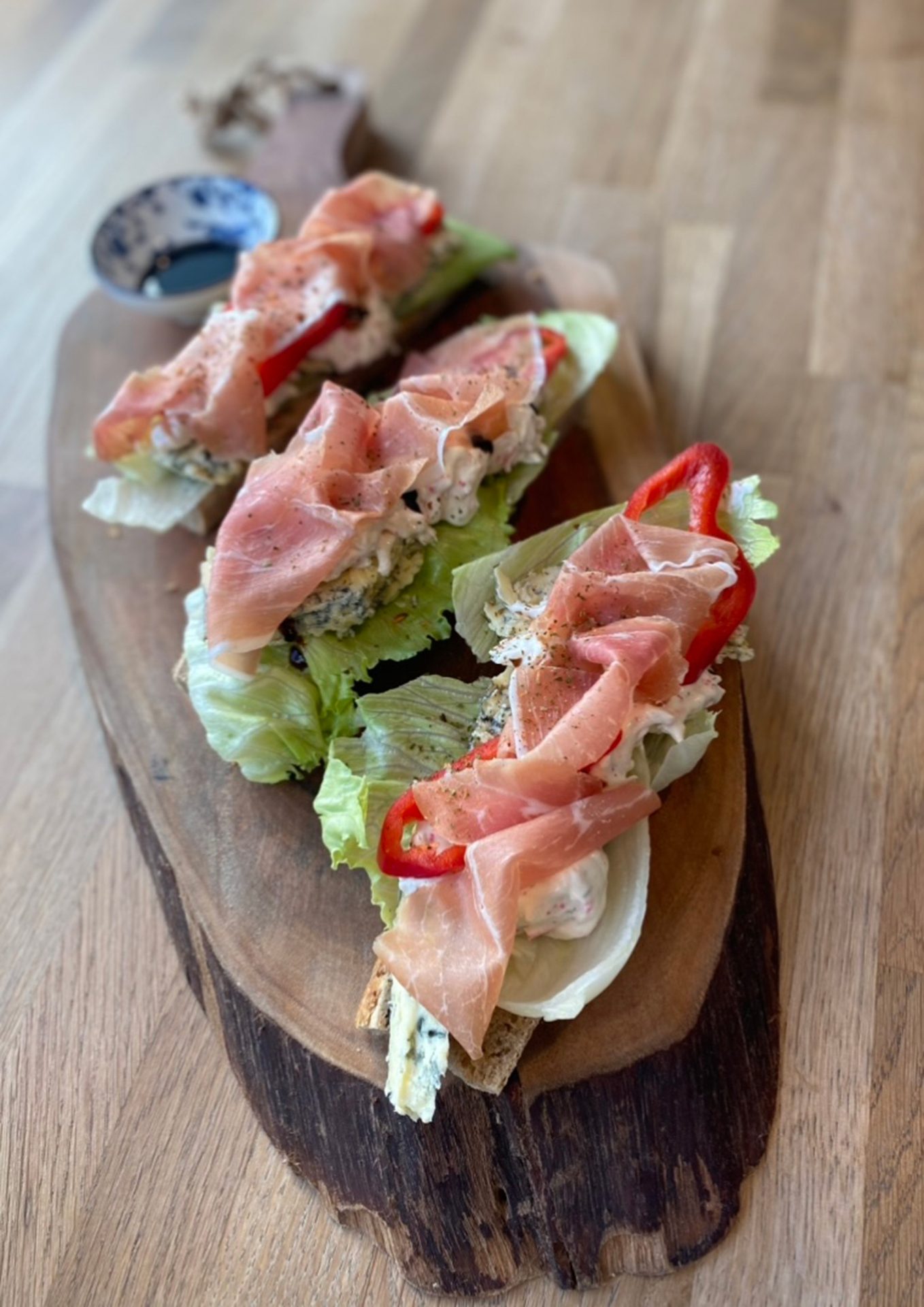 Open-faced sandwiches with prosciutto, lettuce, and red pepper on a wooden board.