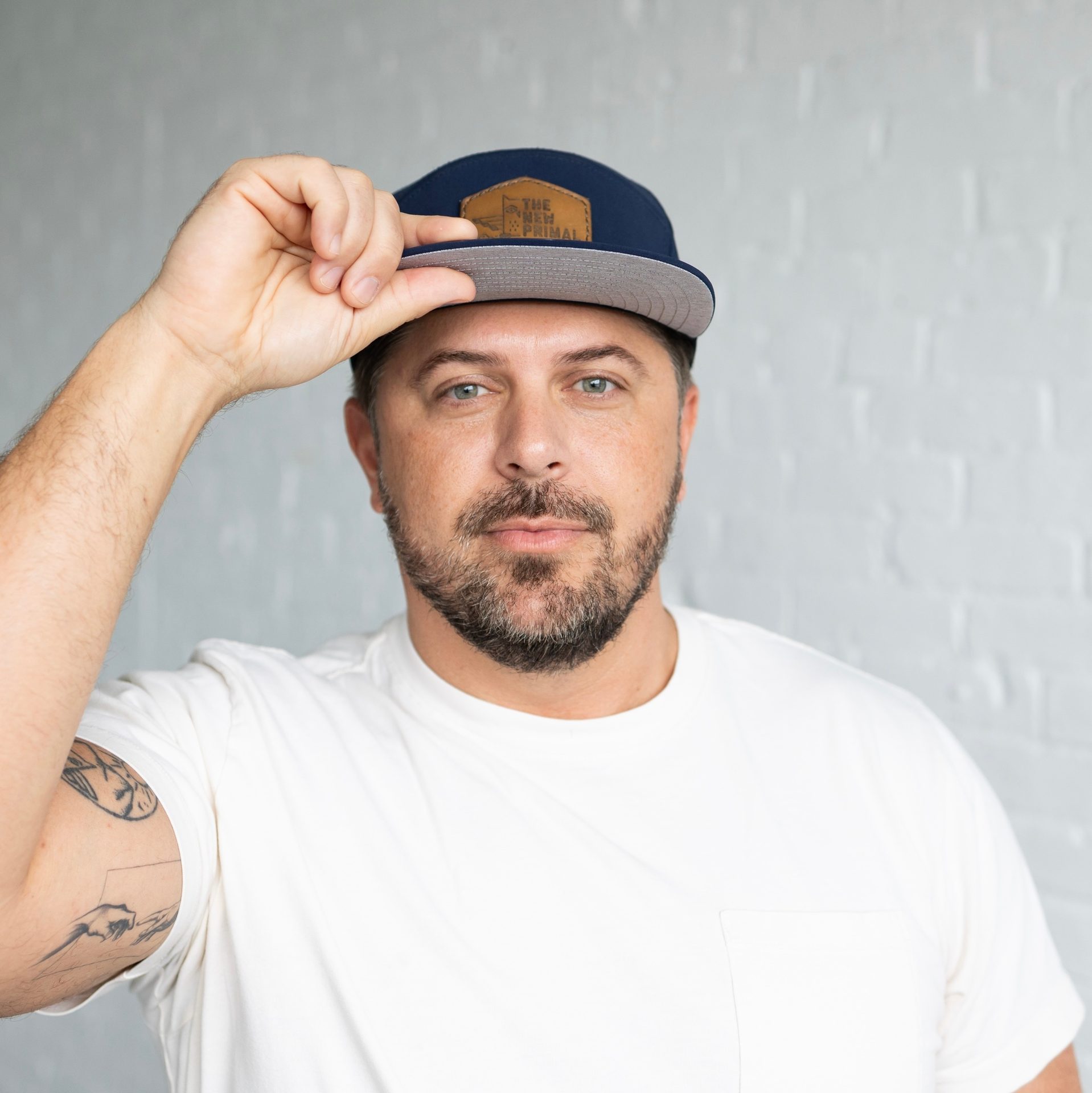 A man wearing a white t-shirt and a blue baseball cap, looking at the camera with a neutral expression.