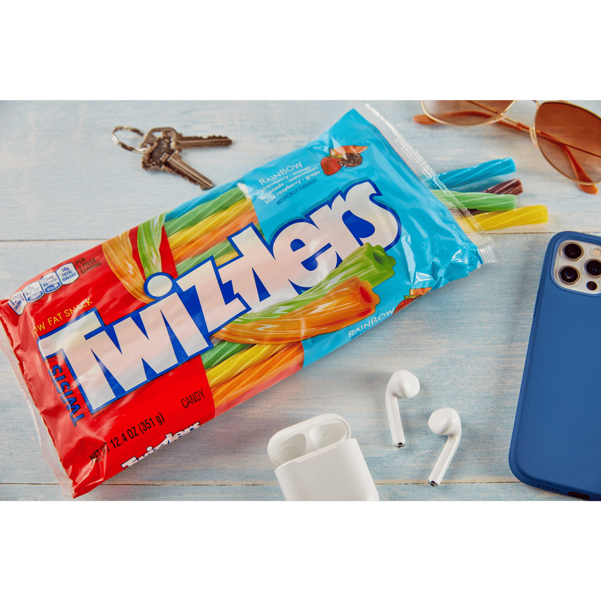 A lifestyle image of a bag of rainbow-colored Twizzlers with car keys, sunglasses, a phone, and earbuds.