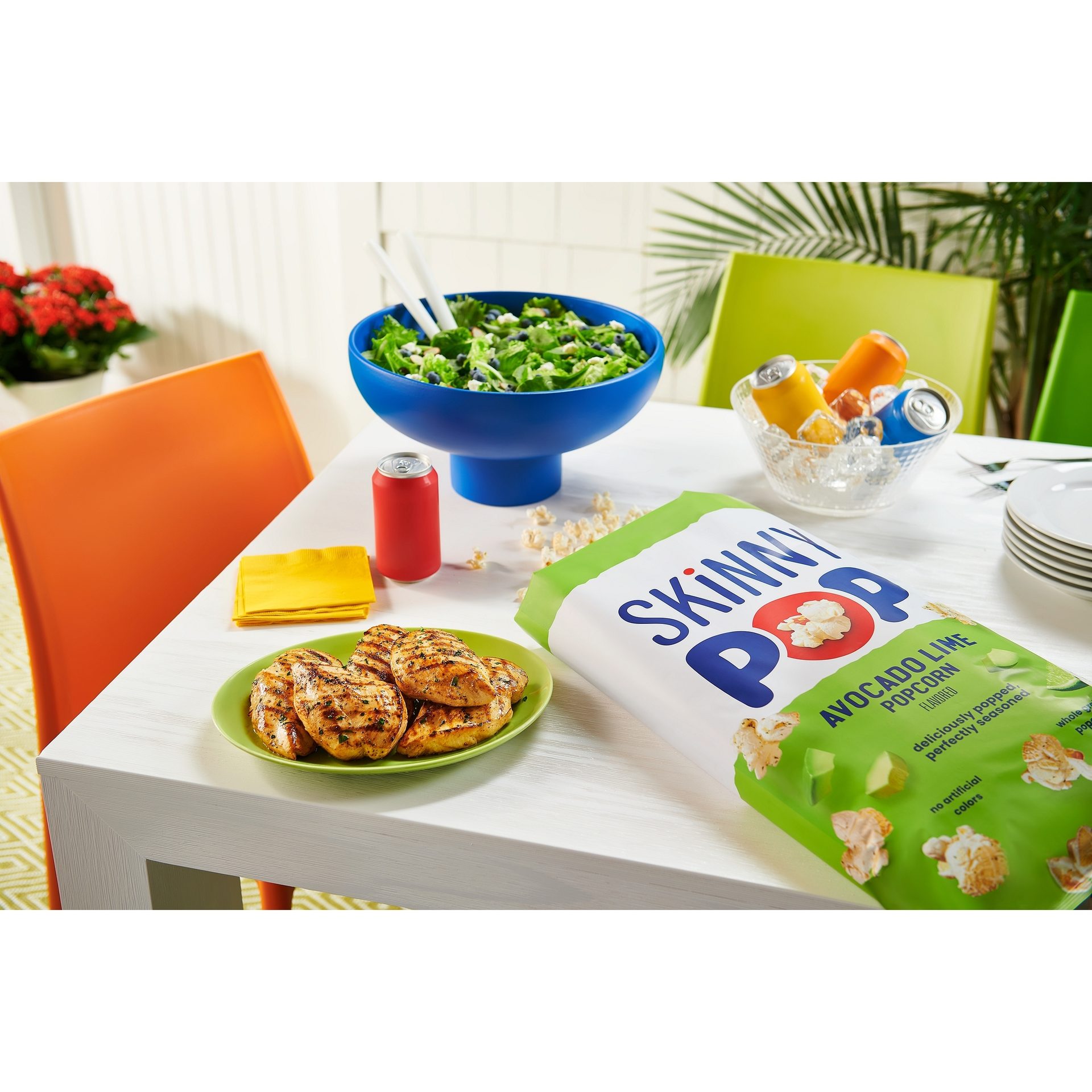 SkinnyPop lifestyle photo with a bag of popcorn, salad, beverages, and grilled chicken in background