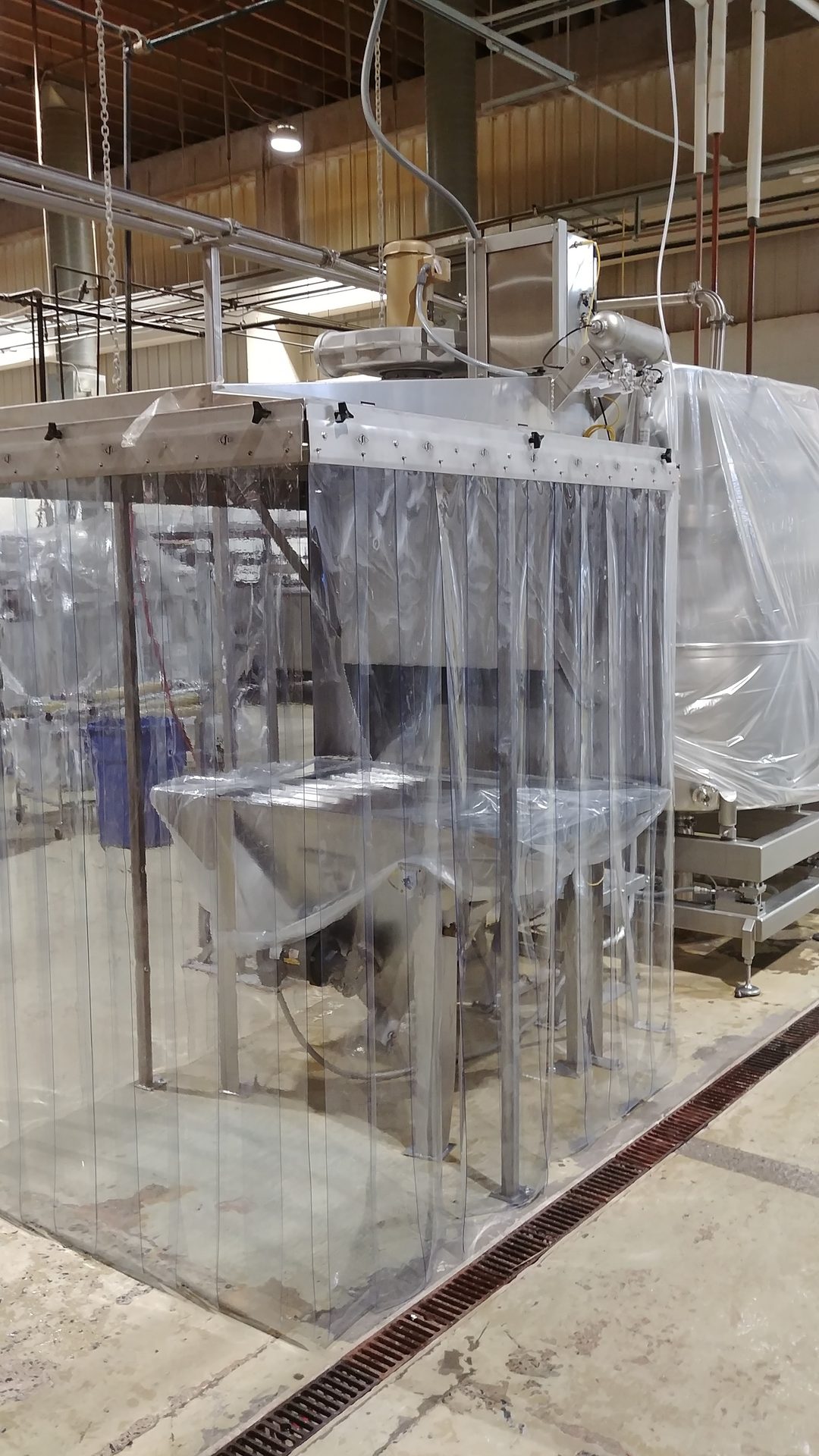Industrial machinery behind clear plastic strip curtains in a factory setting.