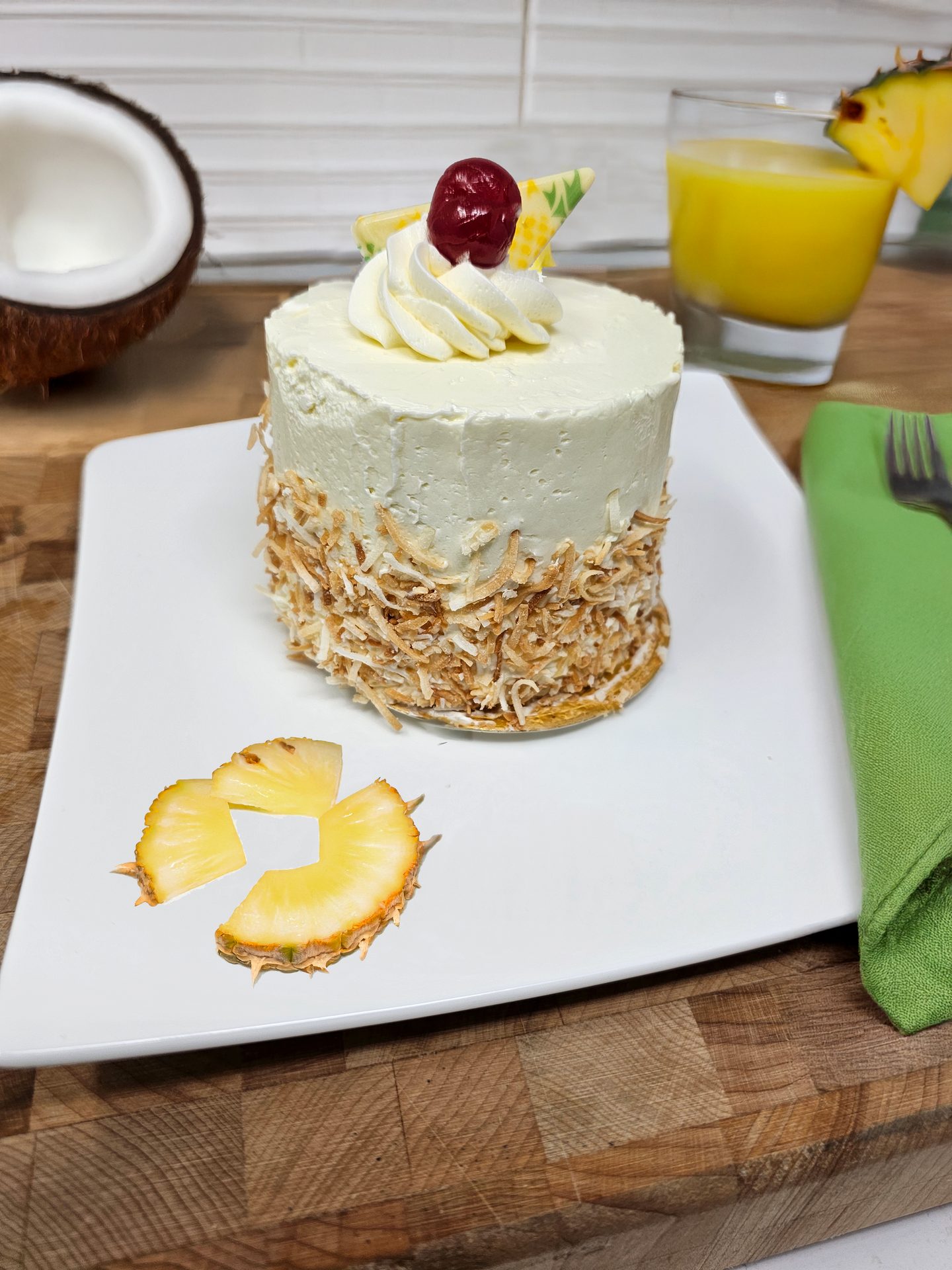 Pina Colada cake with coconut, pineapple, cherry, and juice on a wooden board.
