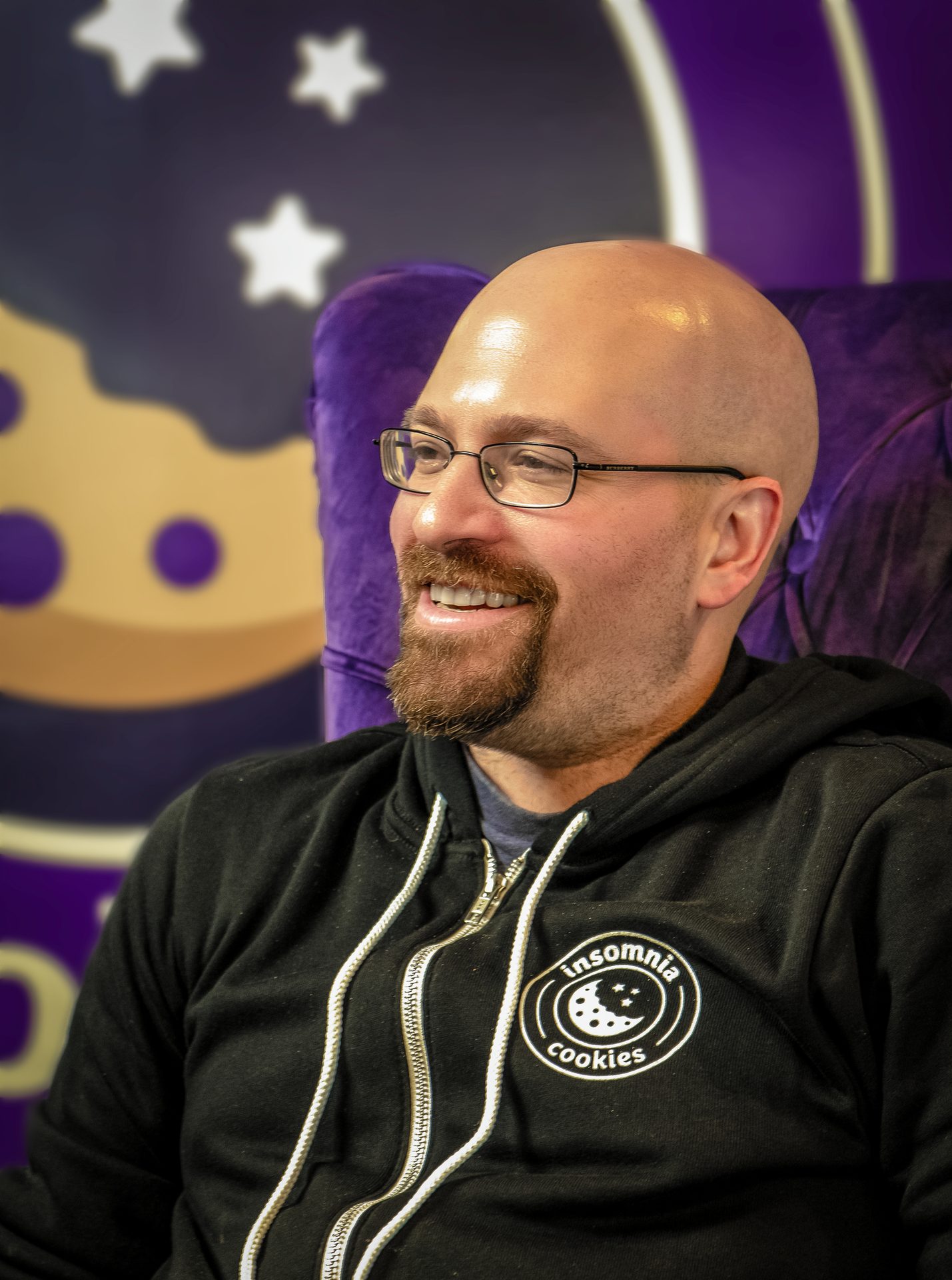 Smiling bald man with glasses and beard, wearing an Insomnia Cookies hoodie.