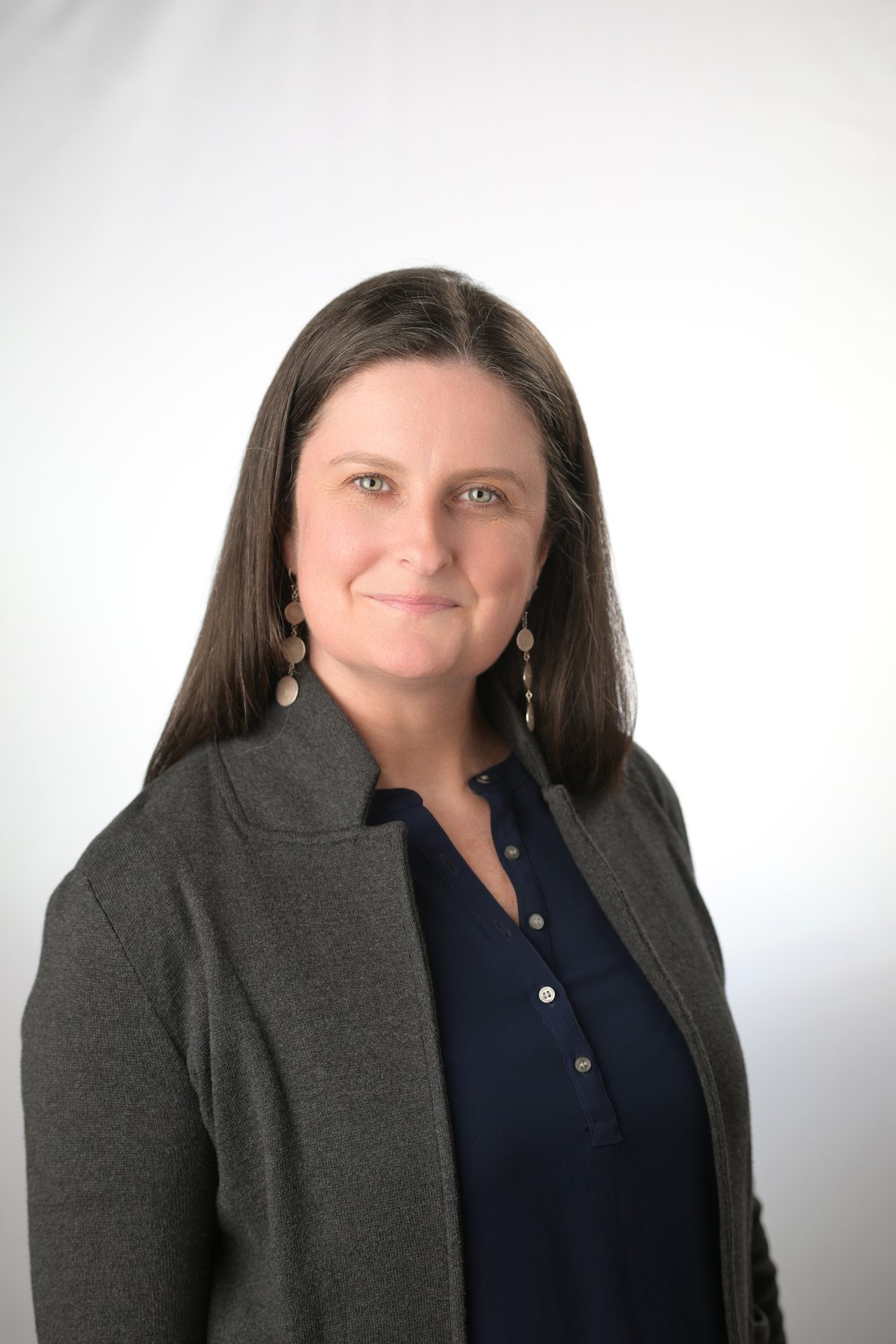 Smiling woman with long dark hair and blue eyes, wearing a grey cardigan over a navy shirt.