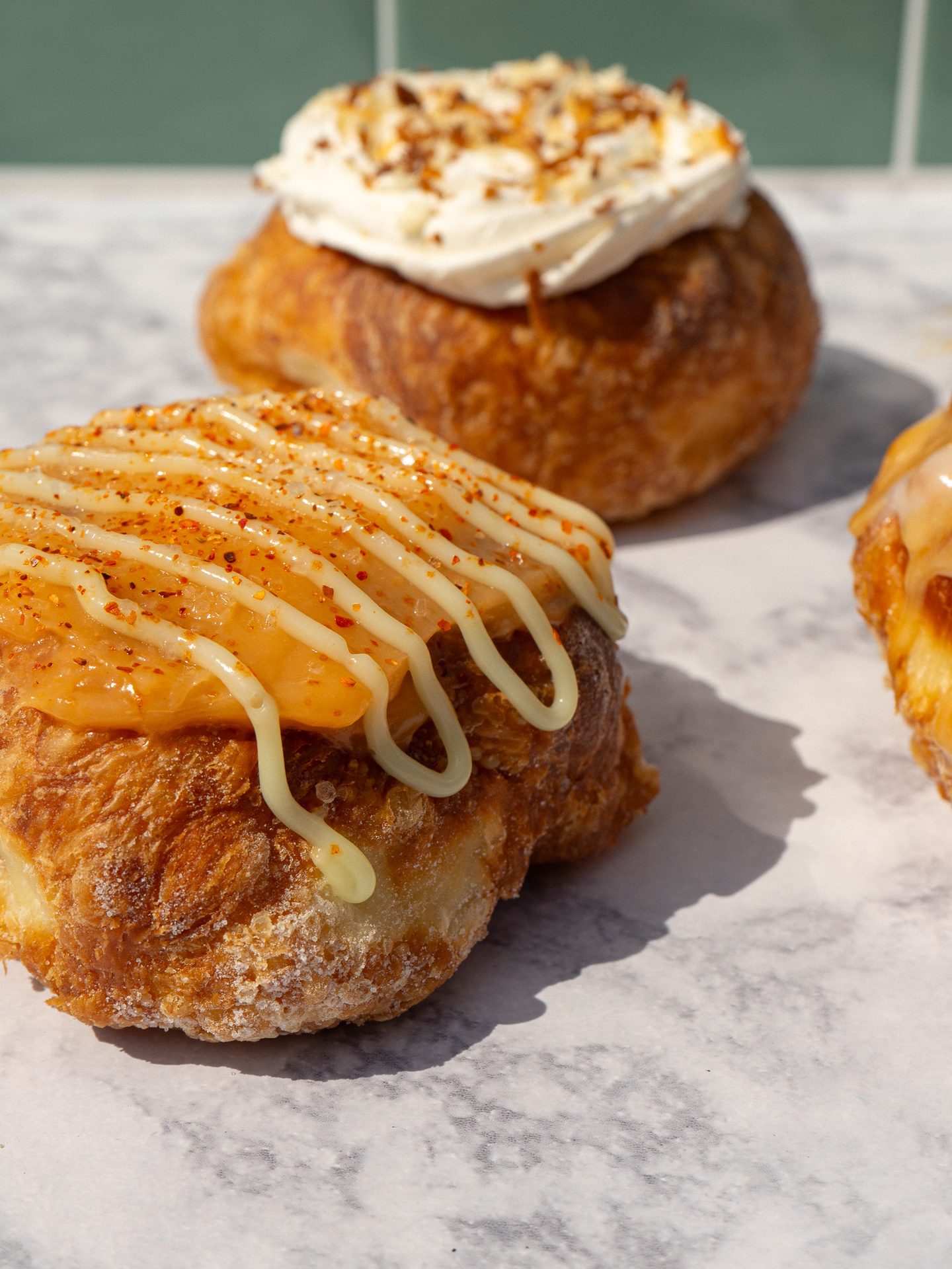 Two gourmet croissants: one with chili-orange drizzle and white stripes, another with cream and nuts, on a marble surface.