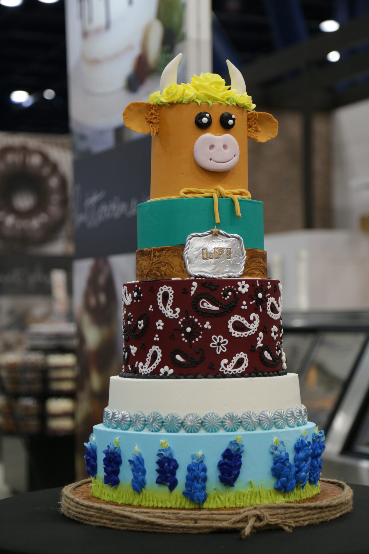 A multi-tiered cake with a cow at the top, at IDDBA 2024