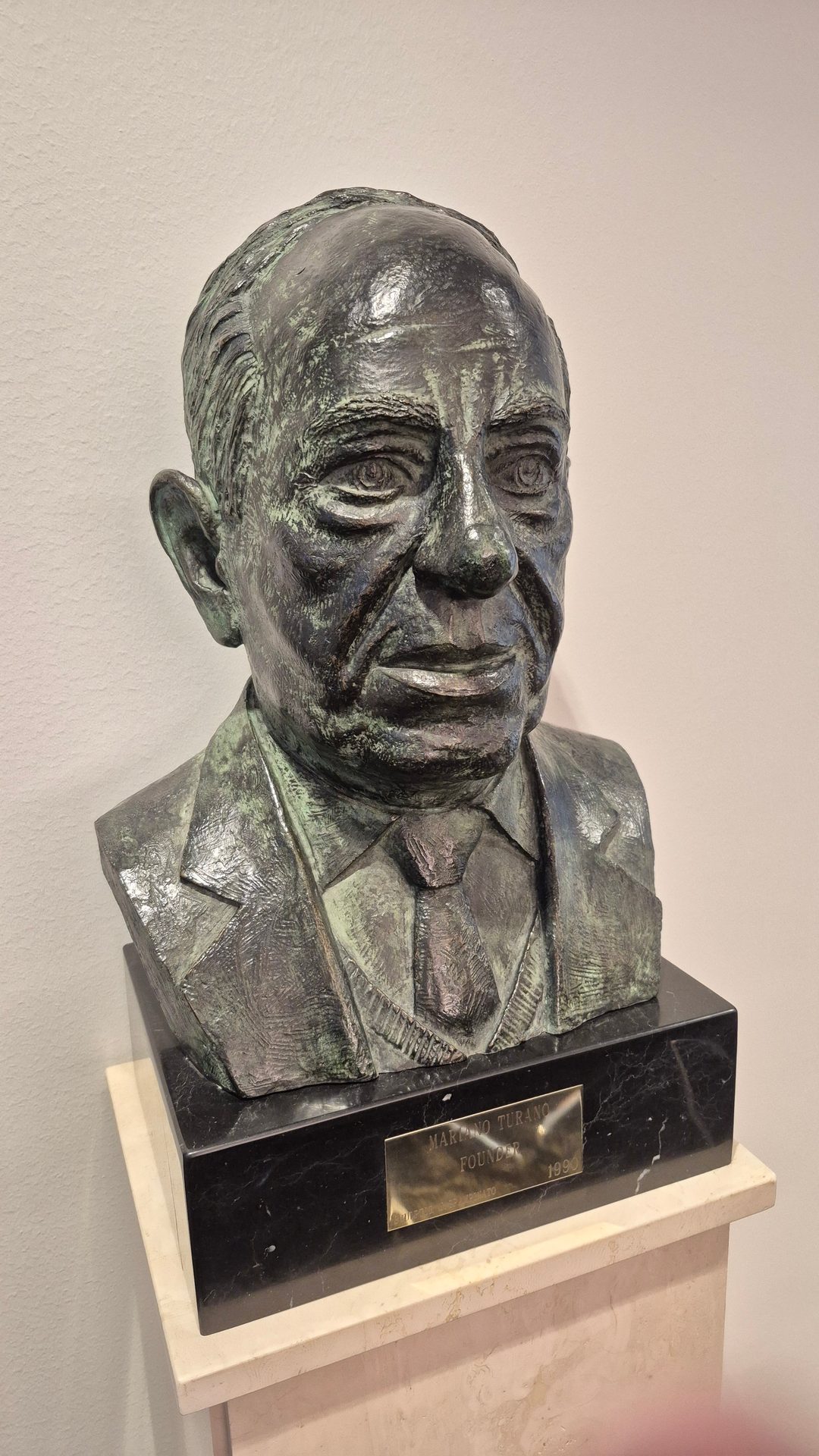 Bronze bust of Mariano Turano, Founder (1990), wearing a suit, on a black marble base.