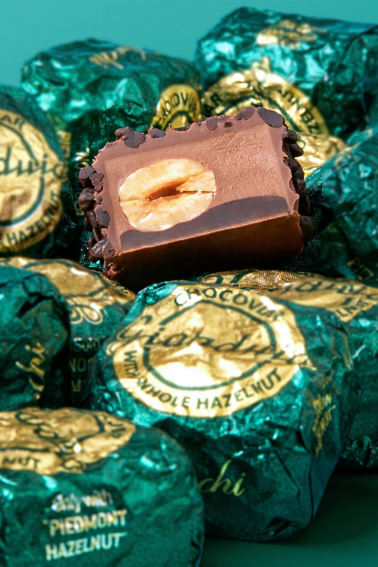 Cut chocolate revealing a whole hazelnut, surrounded by teal and gold foil-wrapped chocolates.