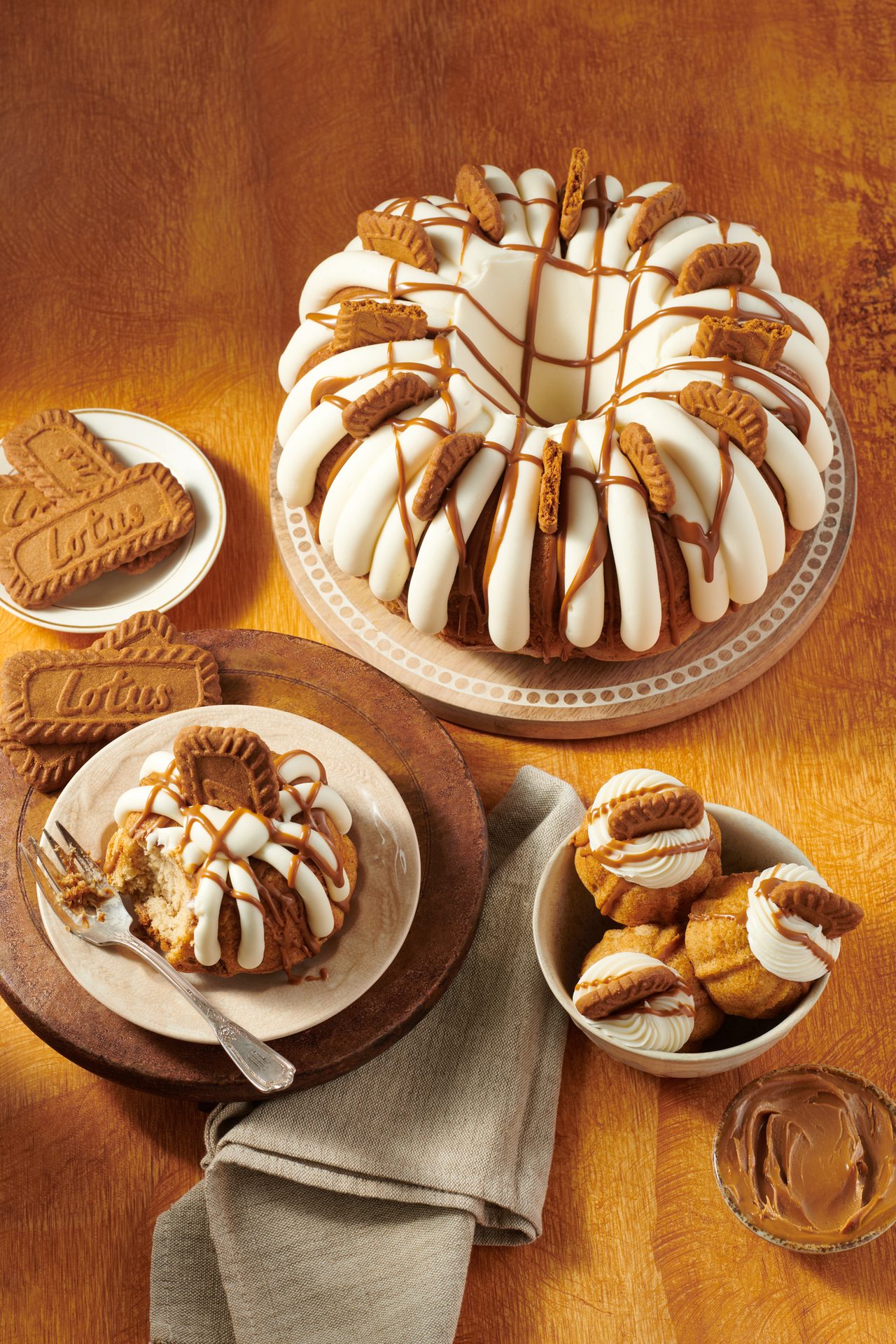 Assortment of bundt cakes and cookies featuring Lotus Biscoff, including a large cake, mini cakes, and a slice.