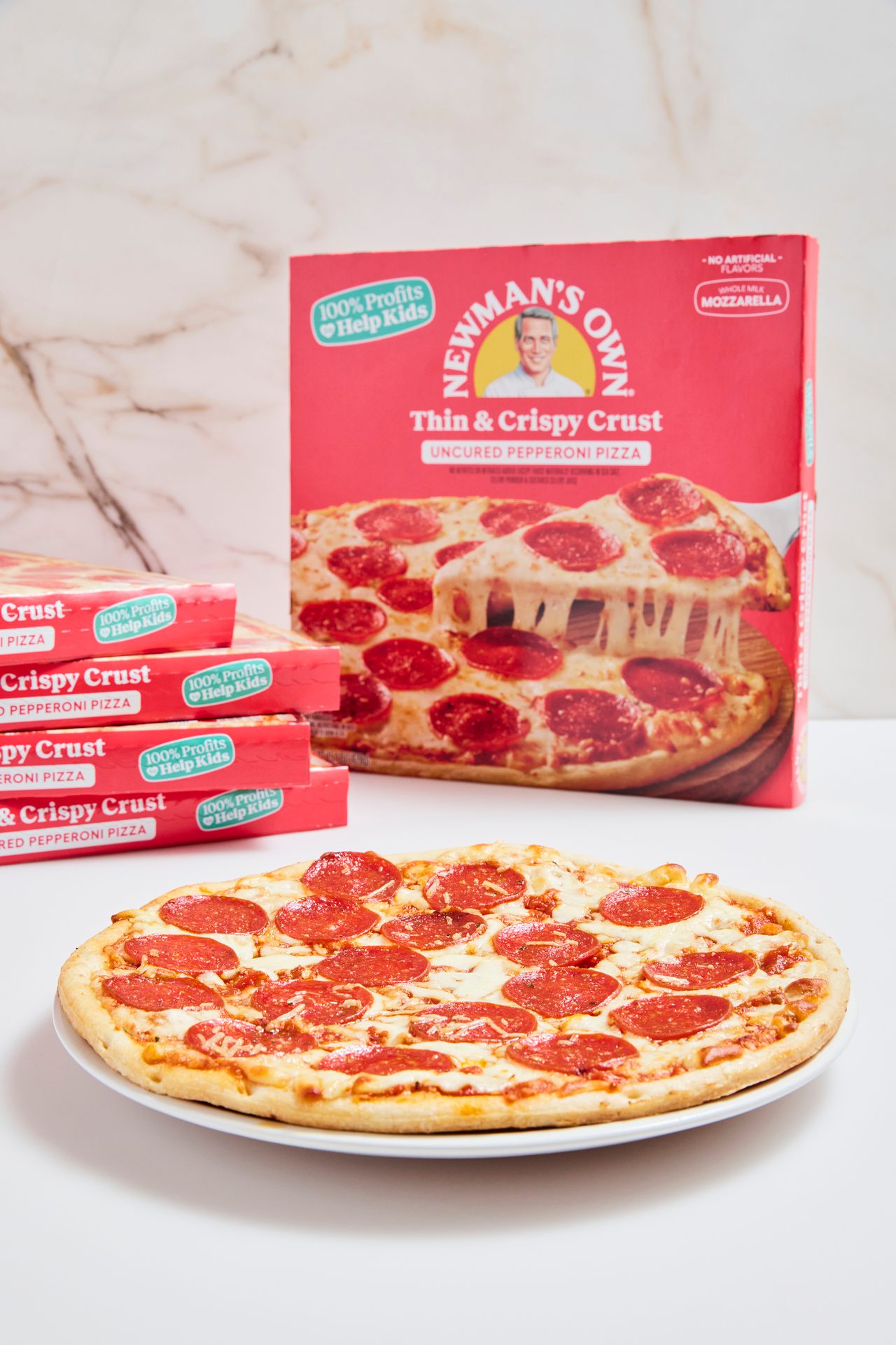 Newman's Own pepperoni pizza on a white plate with boxes showing "100% Profits Help Kids."