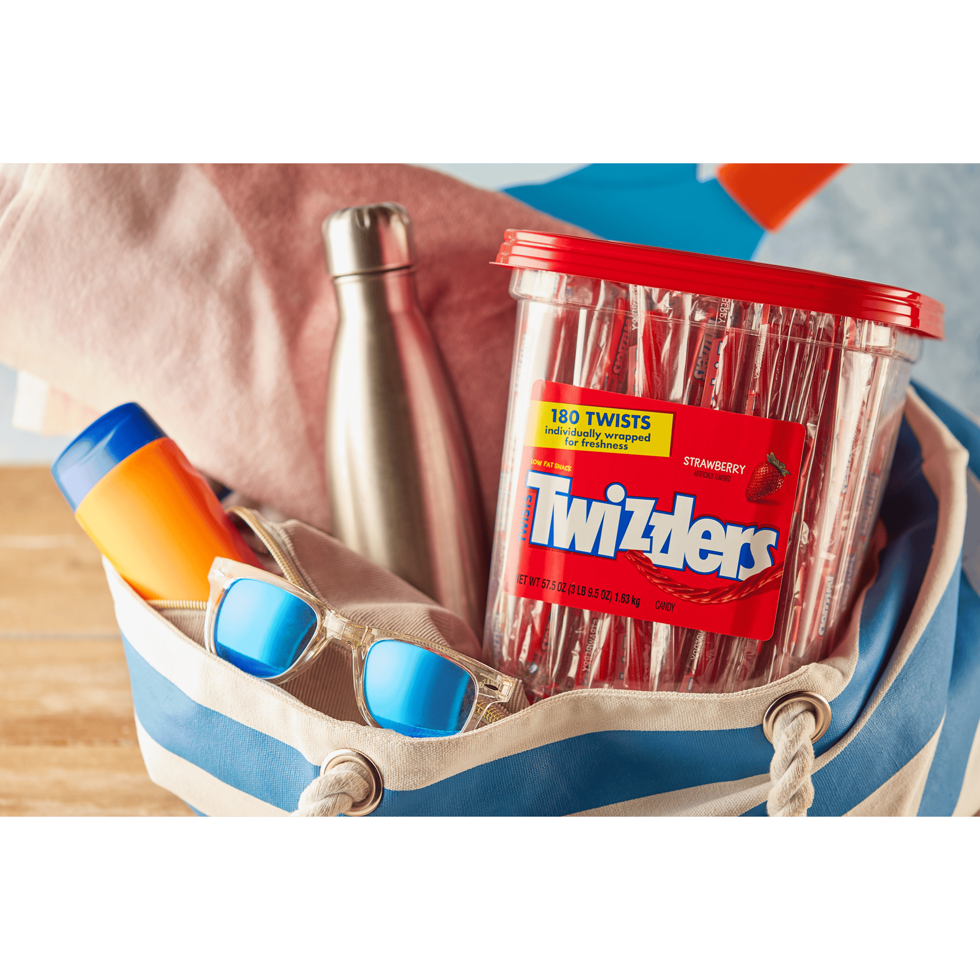 A bulk box of Twizzlers in a summer beach bag along with sunglasses, a water bottle, and sunscreen.