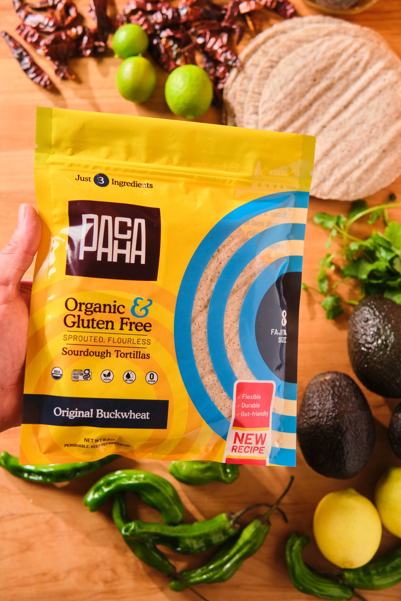 PASA Organic & Gluten-Free Sourdough Tortillas package with ingredients like avocados, peppers, and limes on a wooden table.